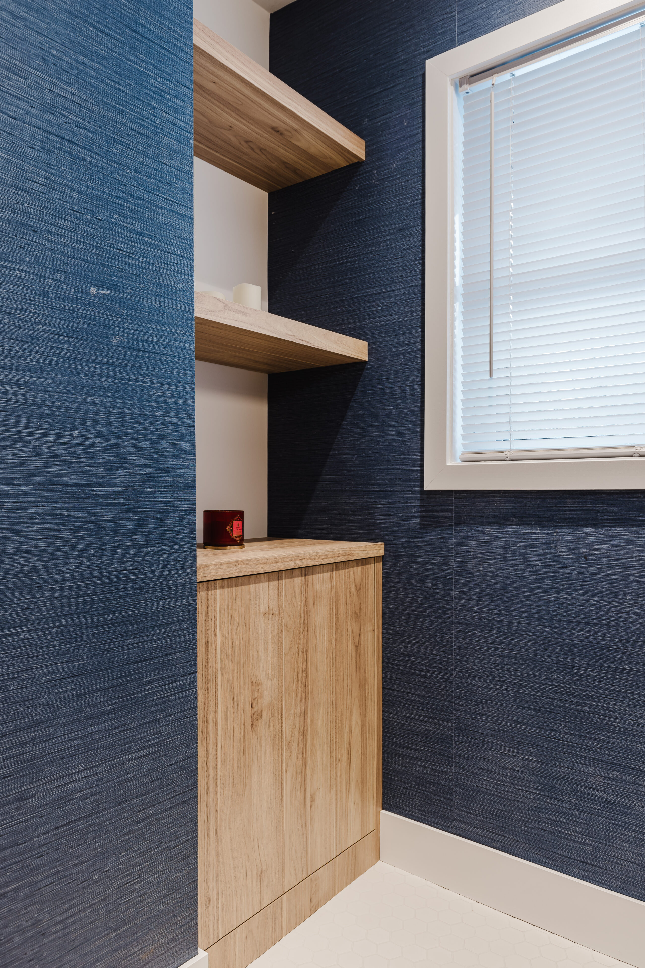 A modern corner features rich blue wallpaper, light wood shelves, and a sleek cabinet, creating a stylish and inviting atmosphere.