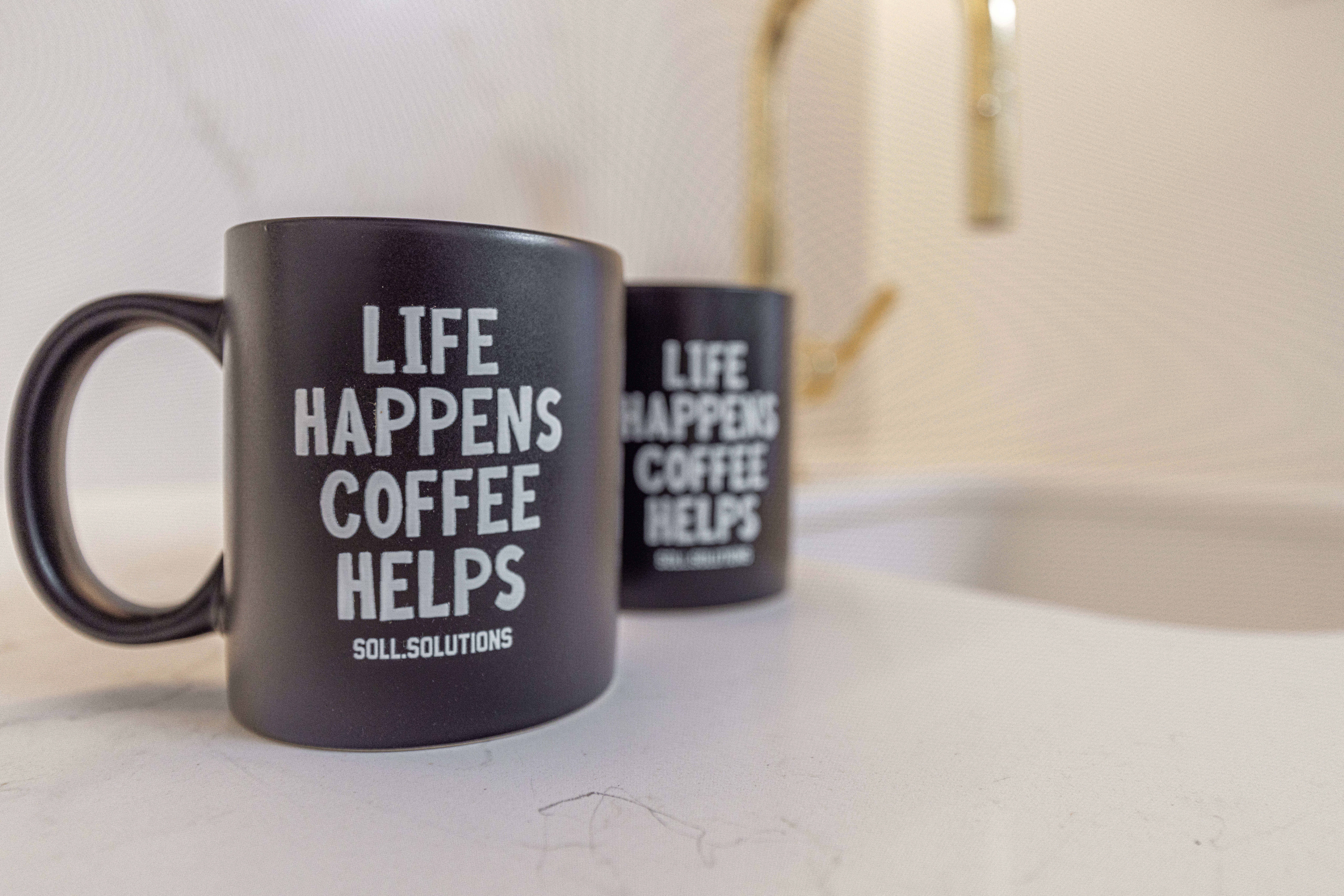 Two matte black coffee mugs with an inspiring quote sit on a bright countertop, perfect for enjoying comforting moments.