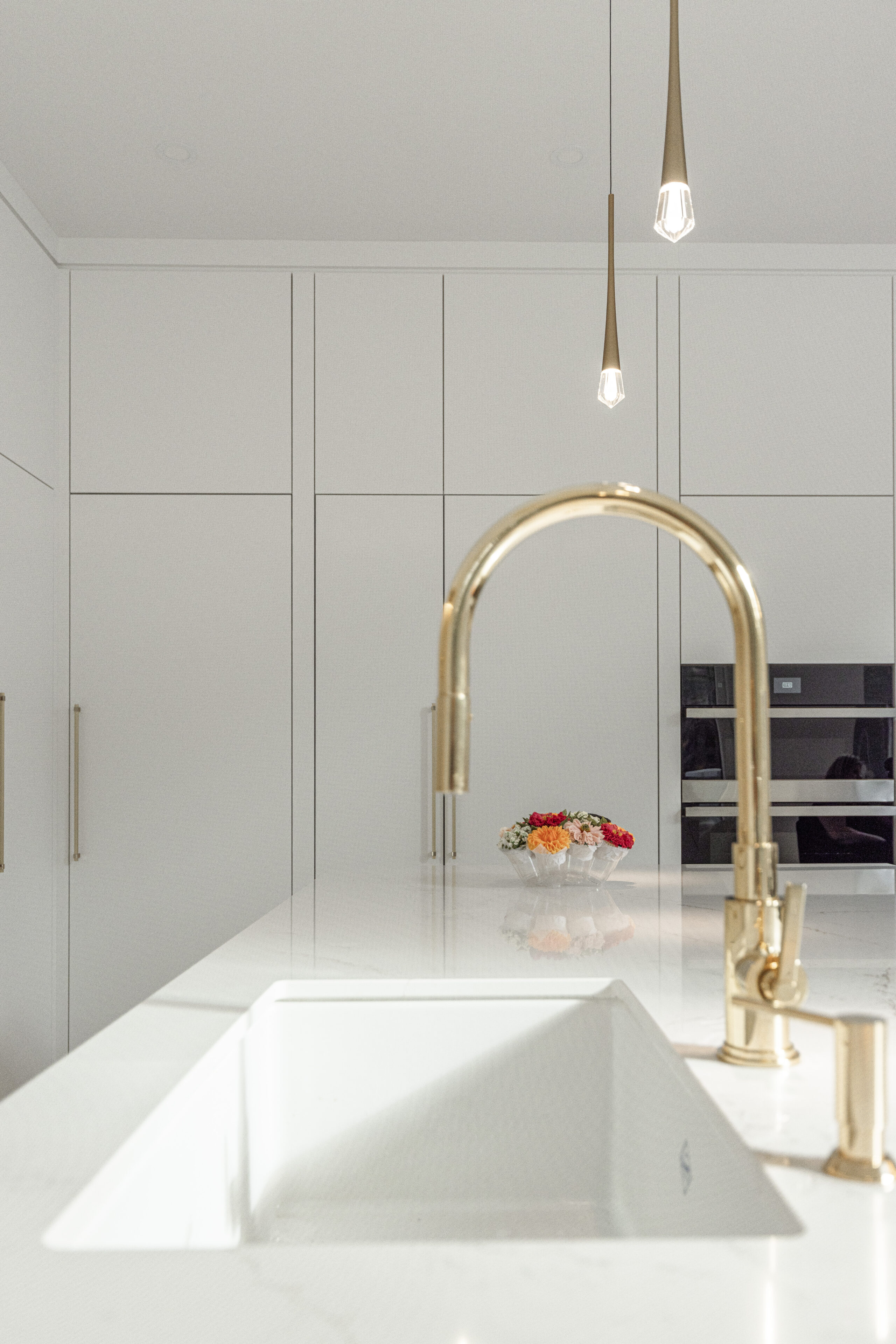 Discover a sleek modern kitchen featuring minimalist white cabinetry, an elegant island with a gold faucet, and stylish pendant lighting.