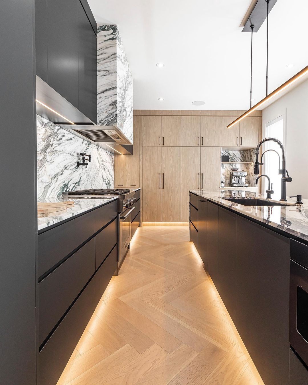 Experience a modern kitchen with sleek black cabinets, a stunning marble backsplash, and elegant herringbone wood flooring for style and functionality.