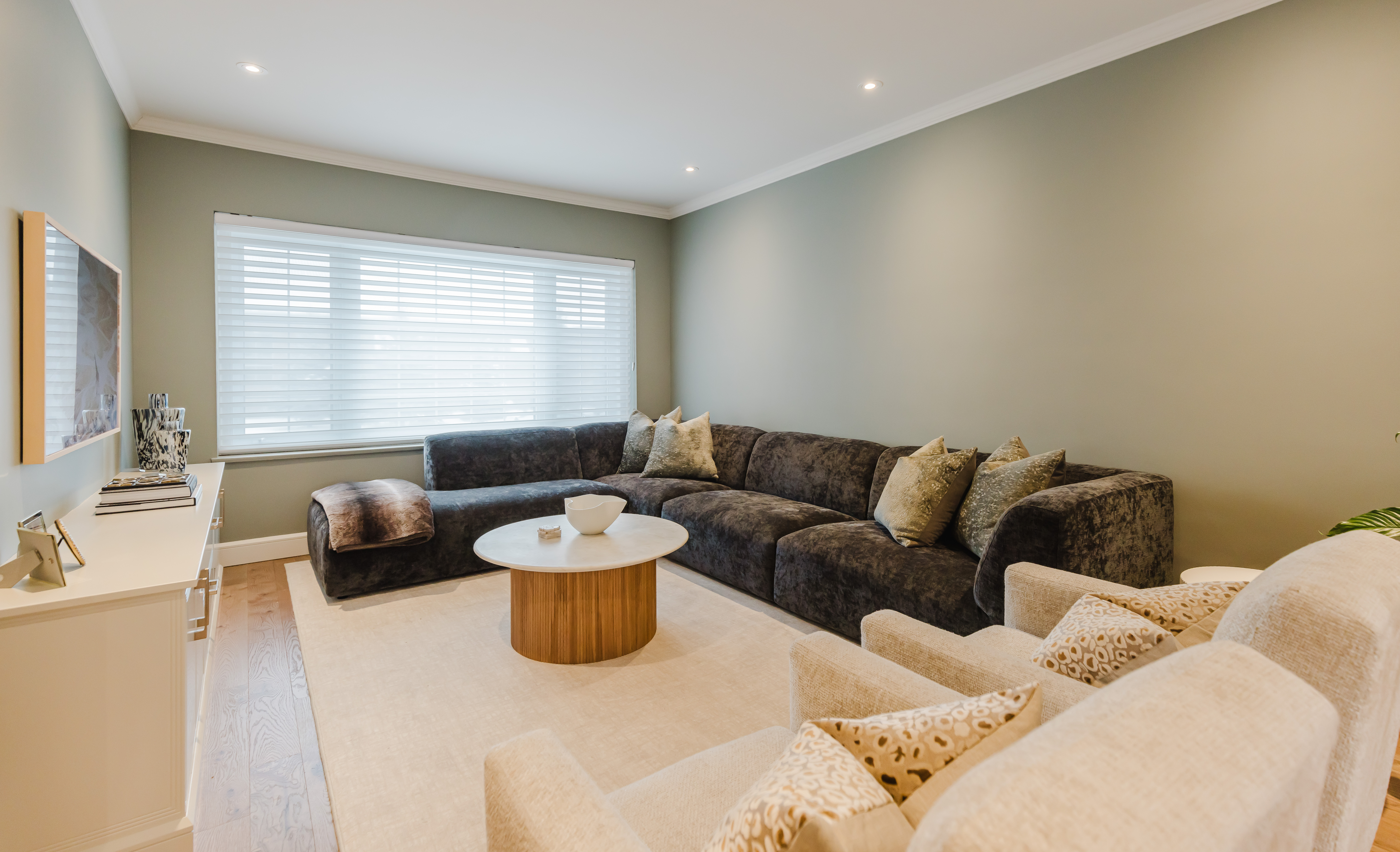 Cozy living room with soft green walls, natural light, and a stylish sectional, perfect for relaxation and social gatherings.