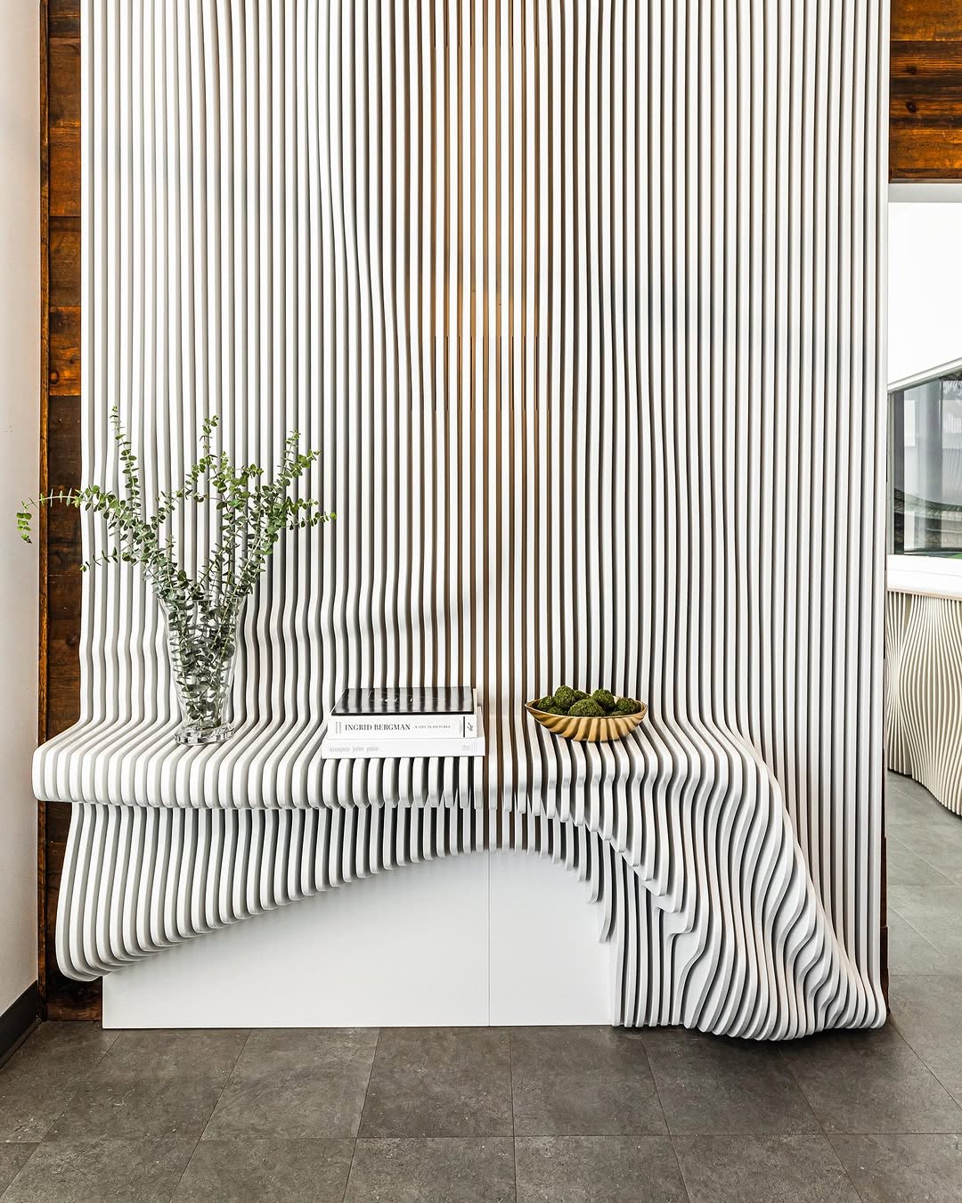 An airy interior features a striped fabric backdrop and a minimalist console table adorned with greenery and curated books.