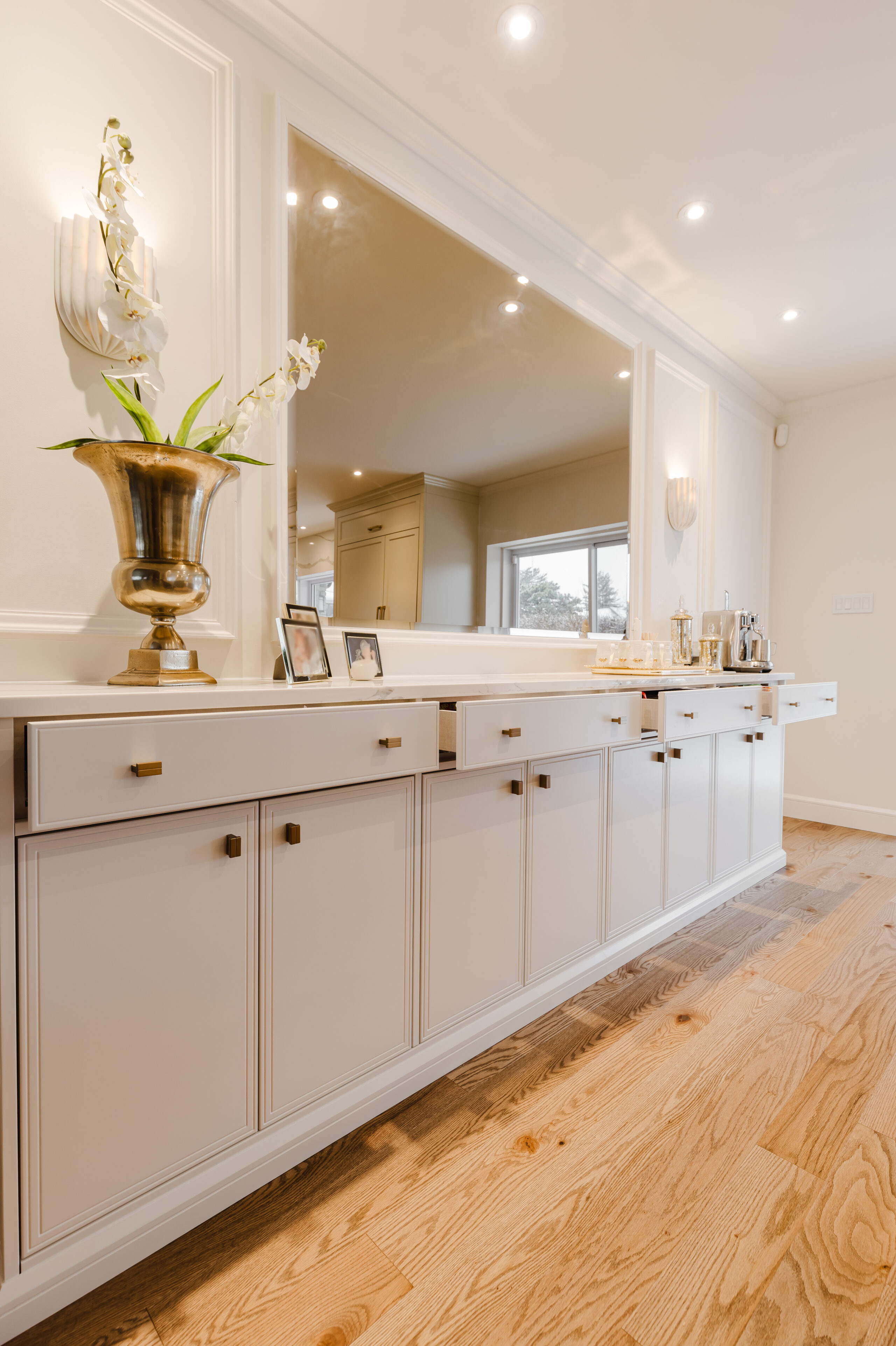 A modern interior features a long white sideboard adorned with greenery and an oversized mirror, creating an elegant and inviting atmosphere.