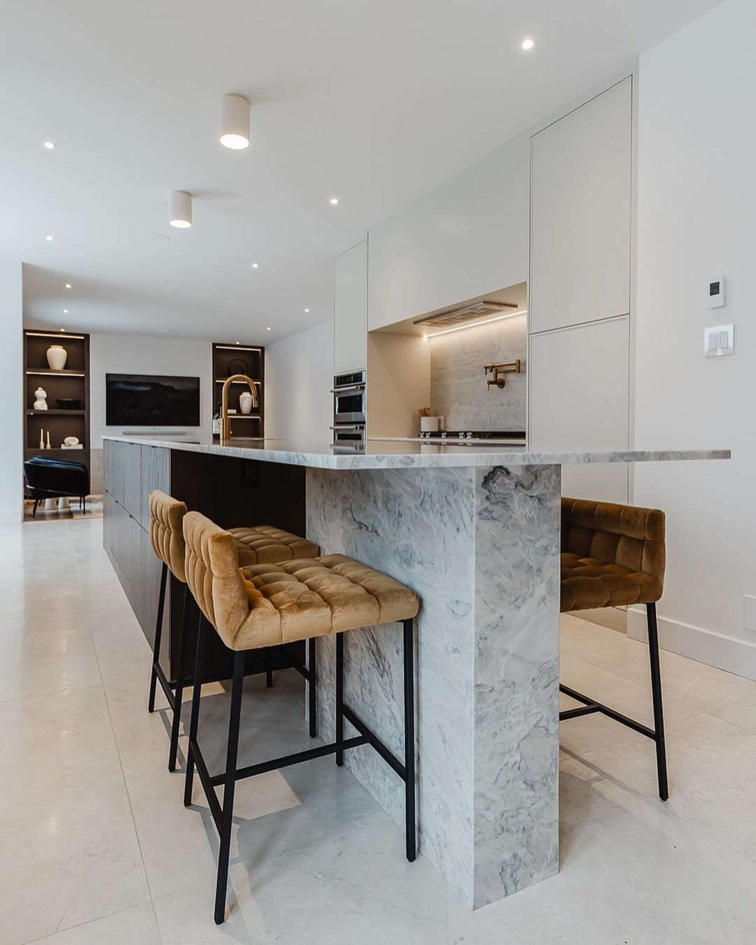 Discover a modern kitchen featuring a stunning marble island, stylish seating, and minimalist cabinetry, all bathed in natural light.