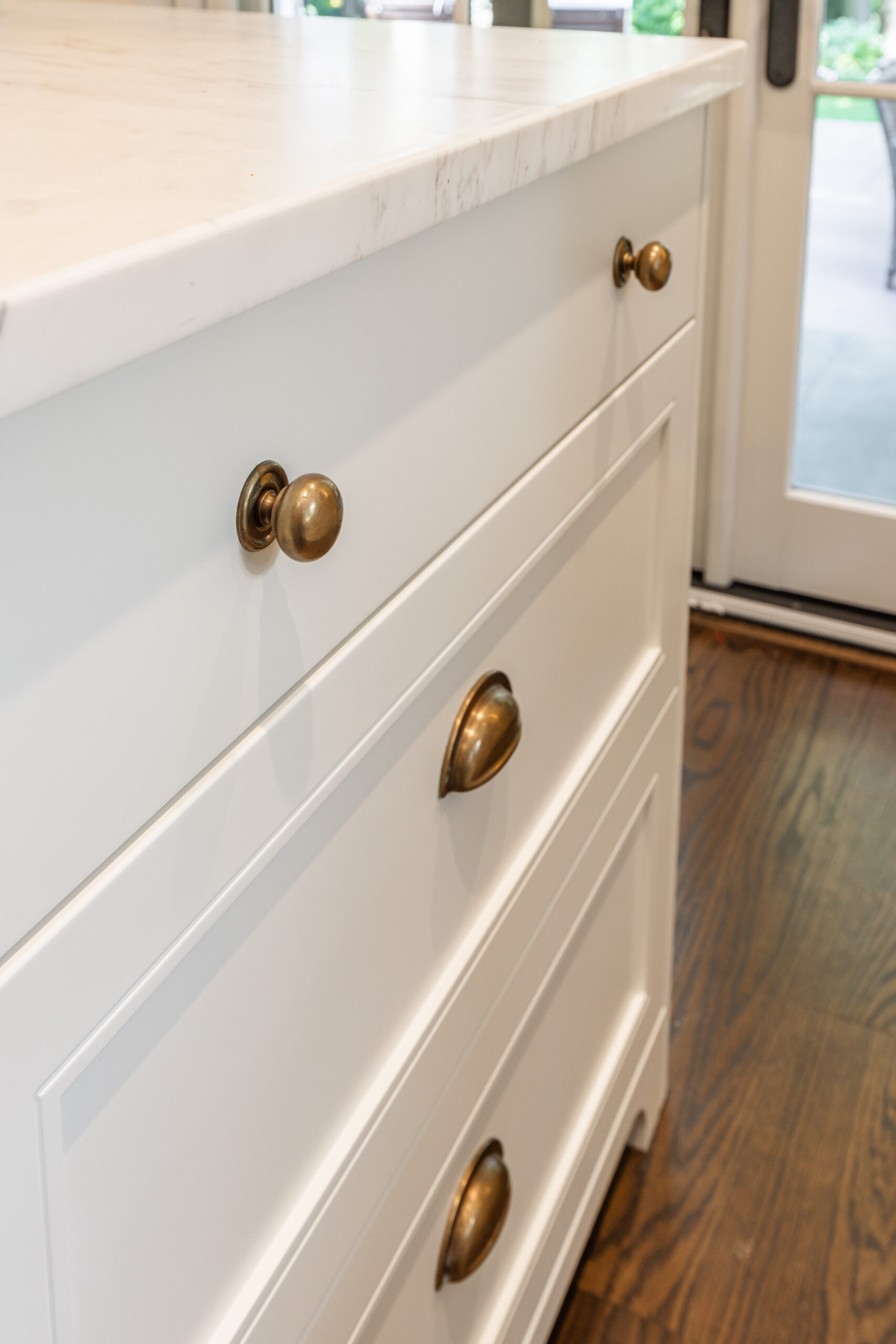 Discover an elegant white kitchen island featuring spacious drawers and antique bronze hardware, illuminated by natural light for a fresh ambiance.