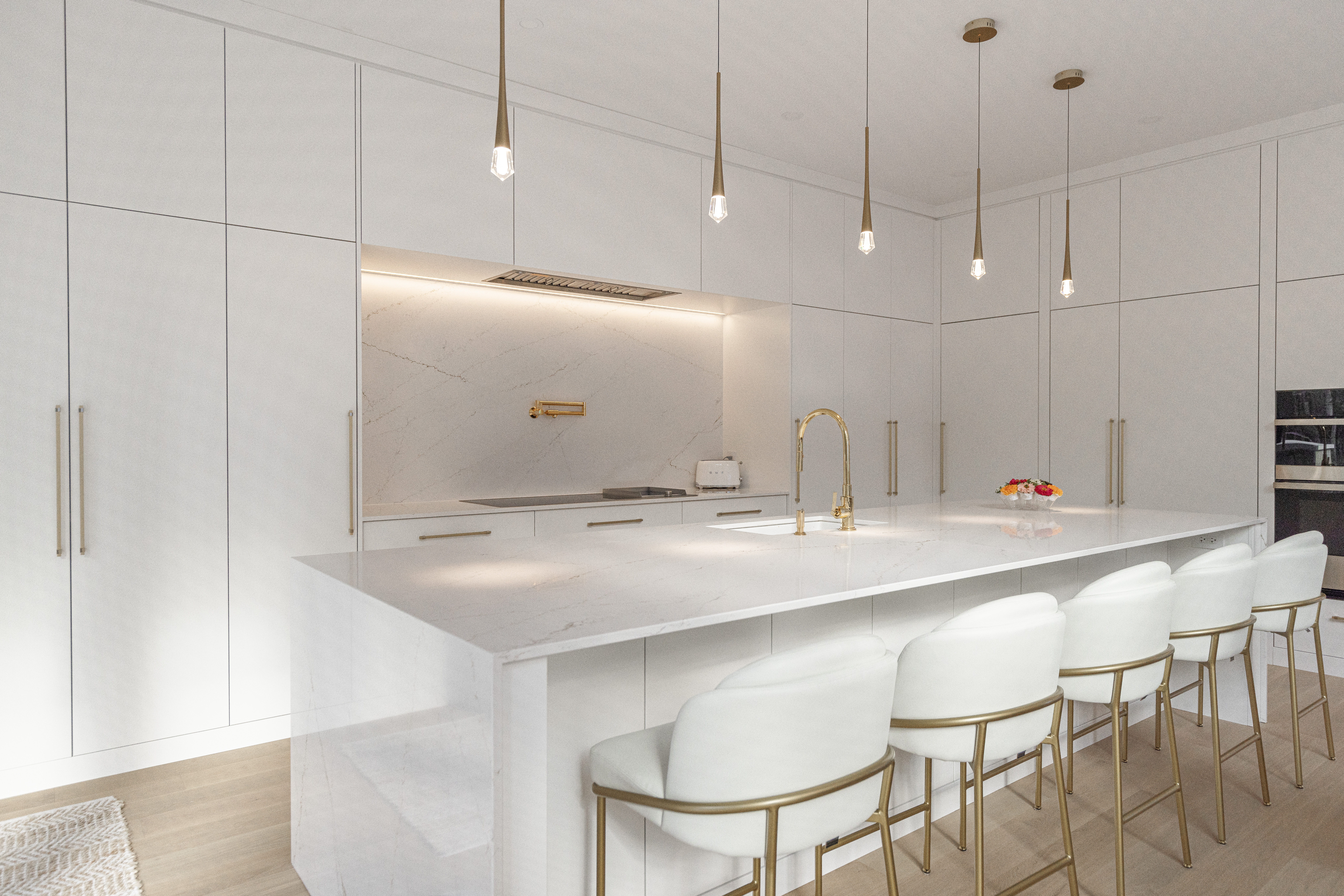Sleek white cabinetry and an elegant island define this modern minimalist kitchen, enhanced by stylish lighting and plush seating.