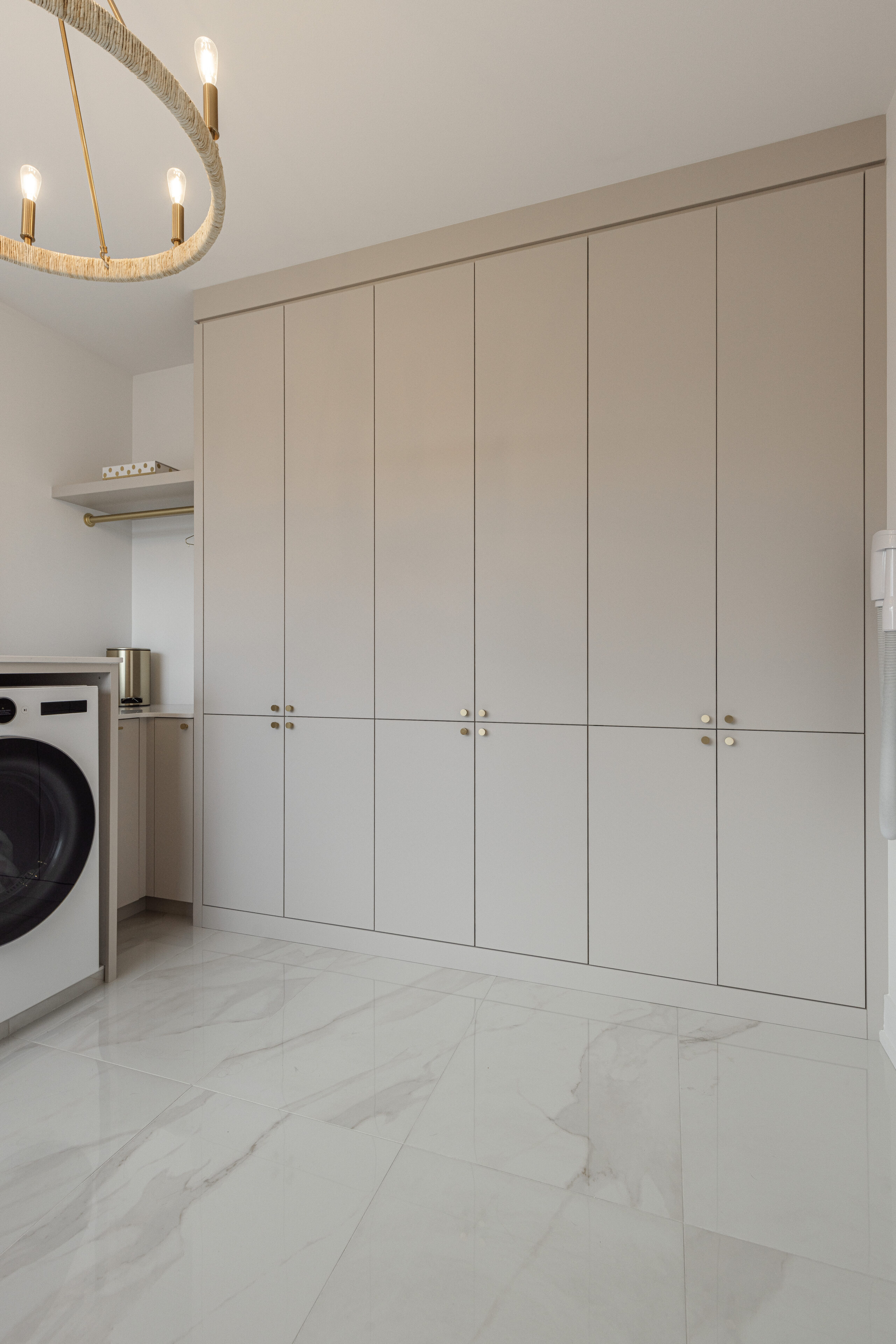 Sleek and organized modern laundry room features stylish cabinetry, a convenient washing machine, and an elegant chandelier for a welcoming ambiance.