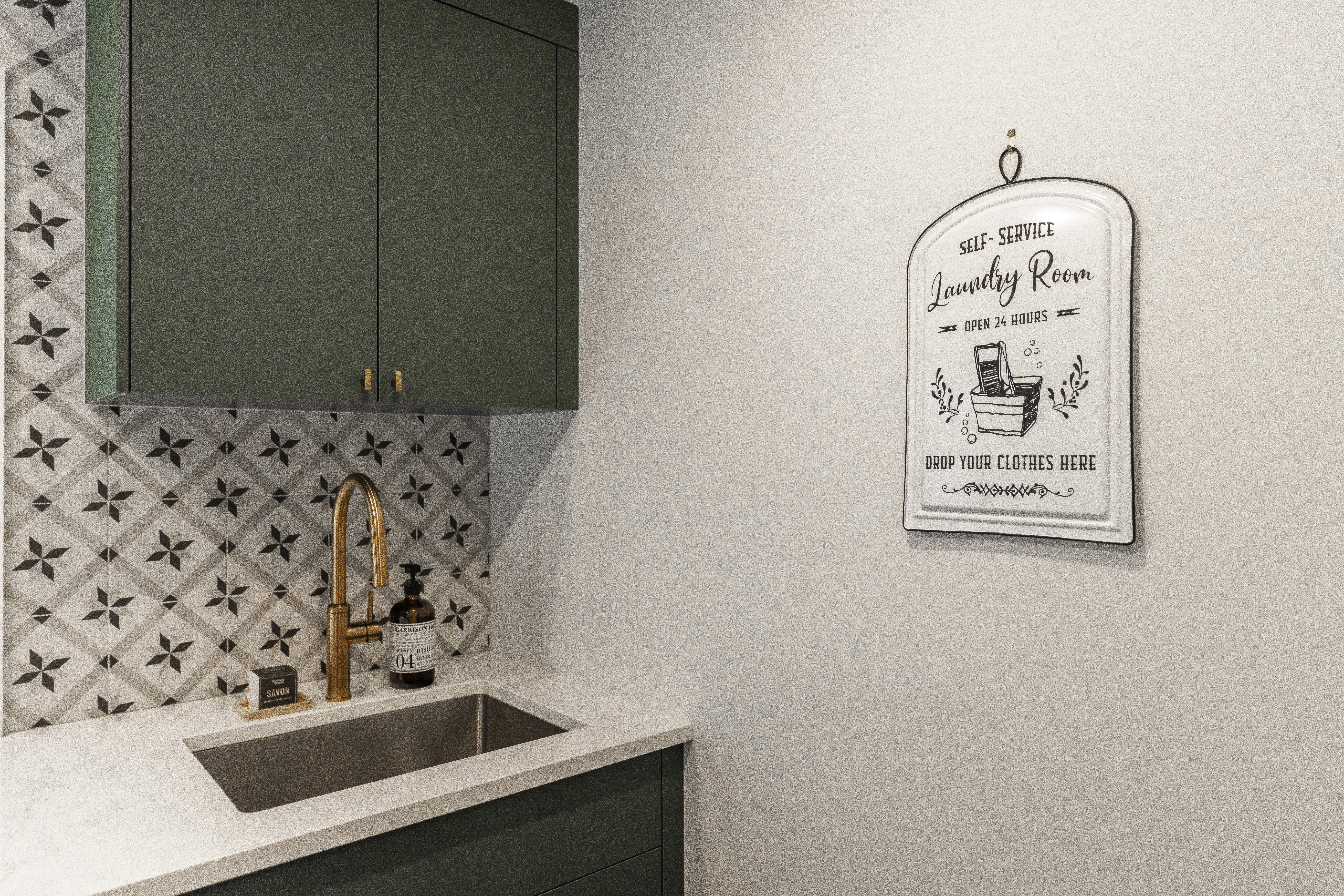 Explore this chic laundry room featuring floral tiles, deep green cabinetry, and a stylish gold-accented sink for a perfect blend of vintage and modern design.