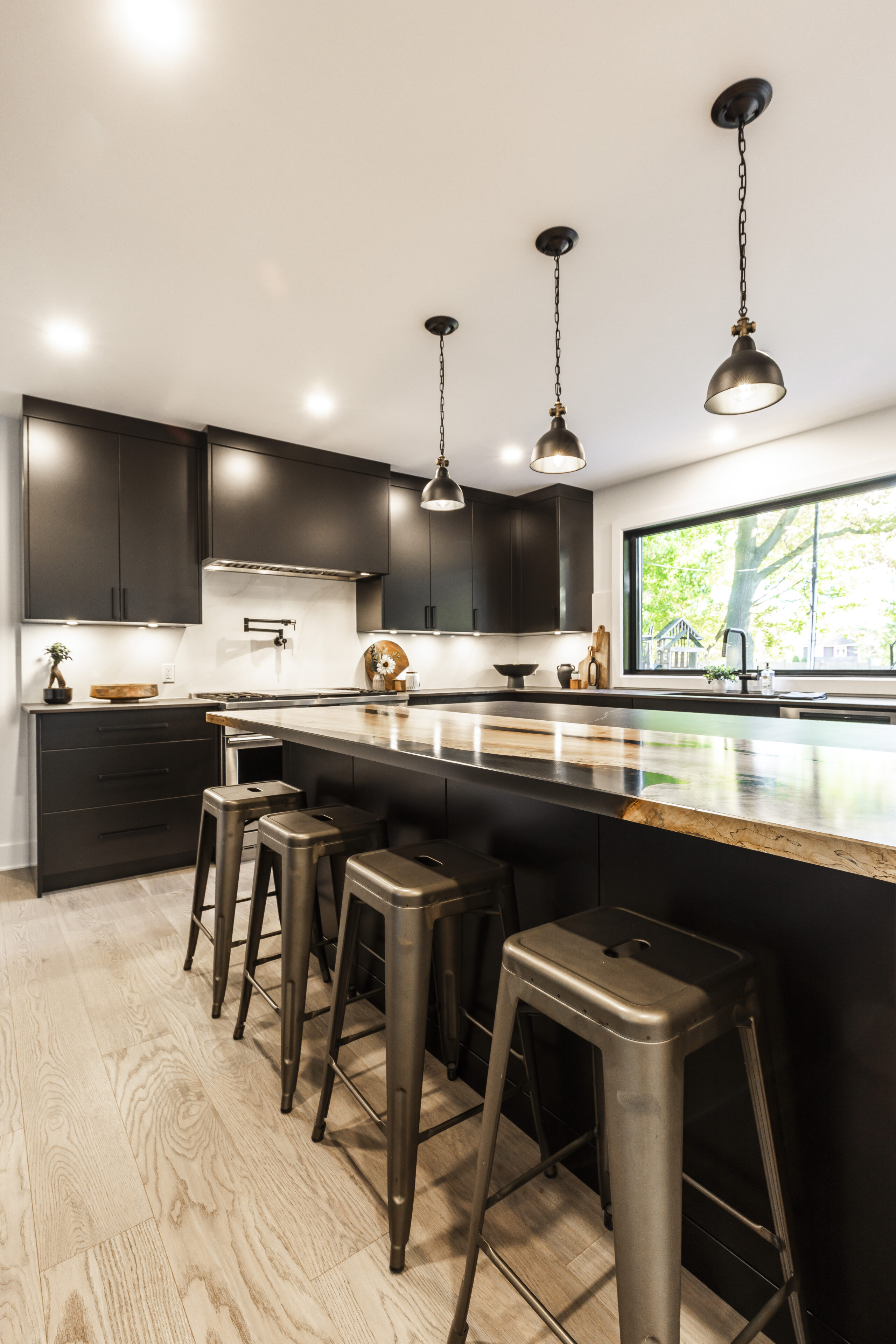 This elegant black kitchen features a natural stone island and large windows that invite light and outdoor views for a welcoming atmosphere.