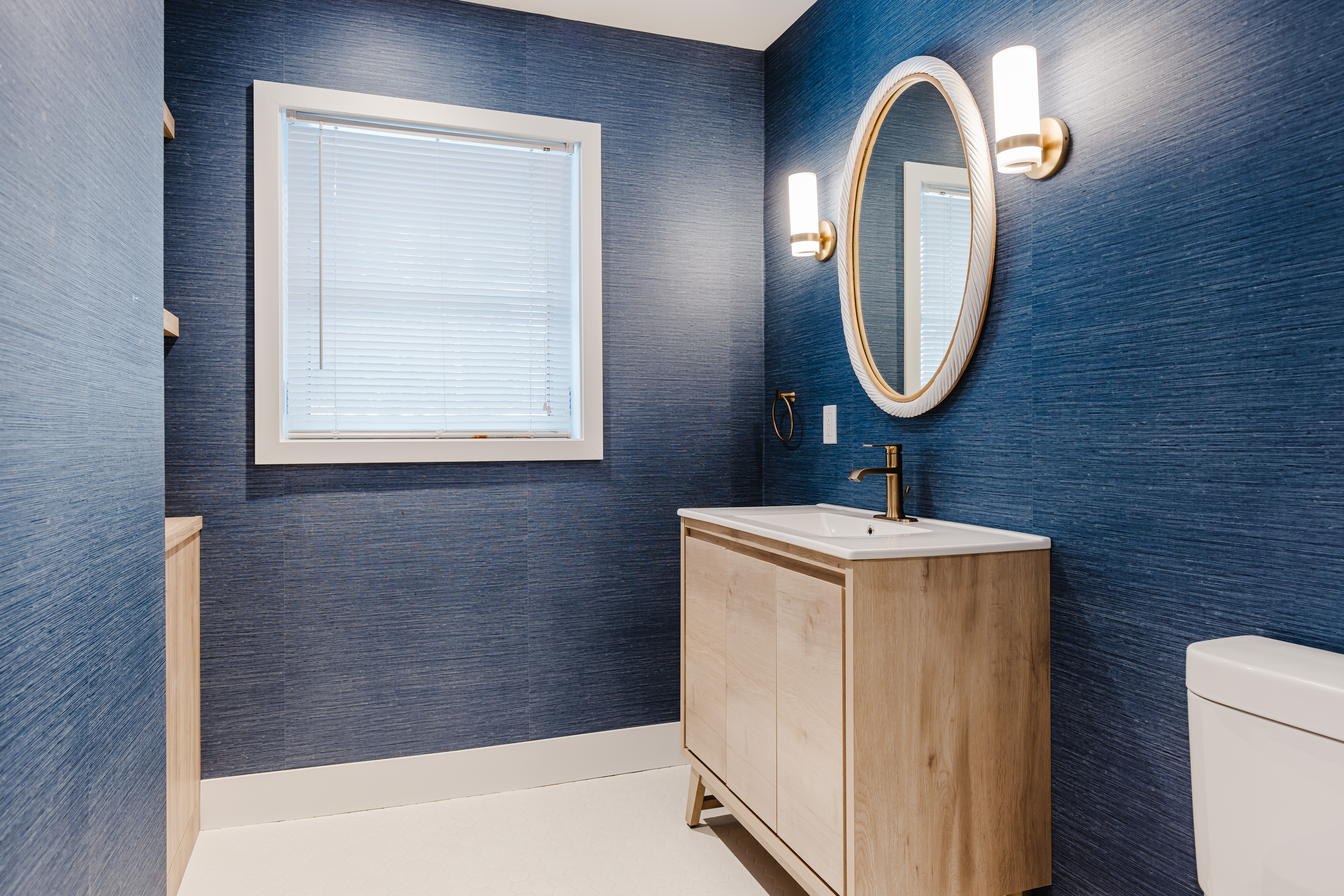Experience luxury in this modern blue bathroom featuring a light wood vanity, gold accents, and abundant natural light.