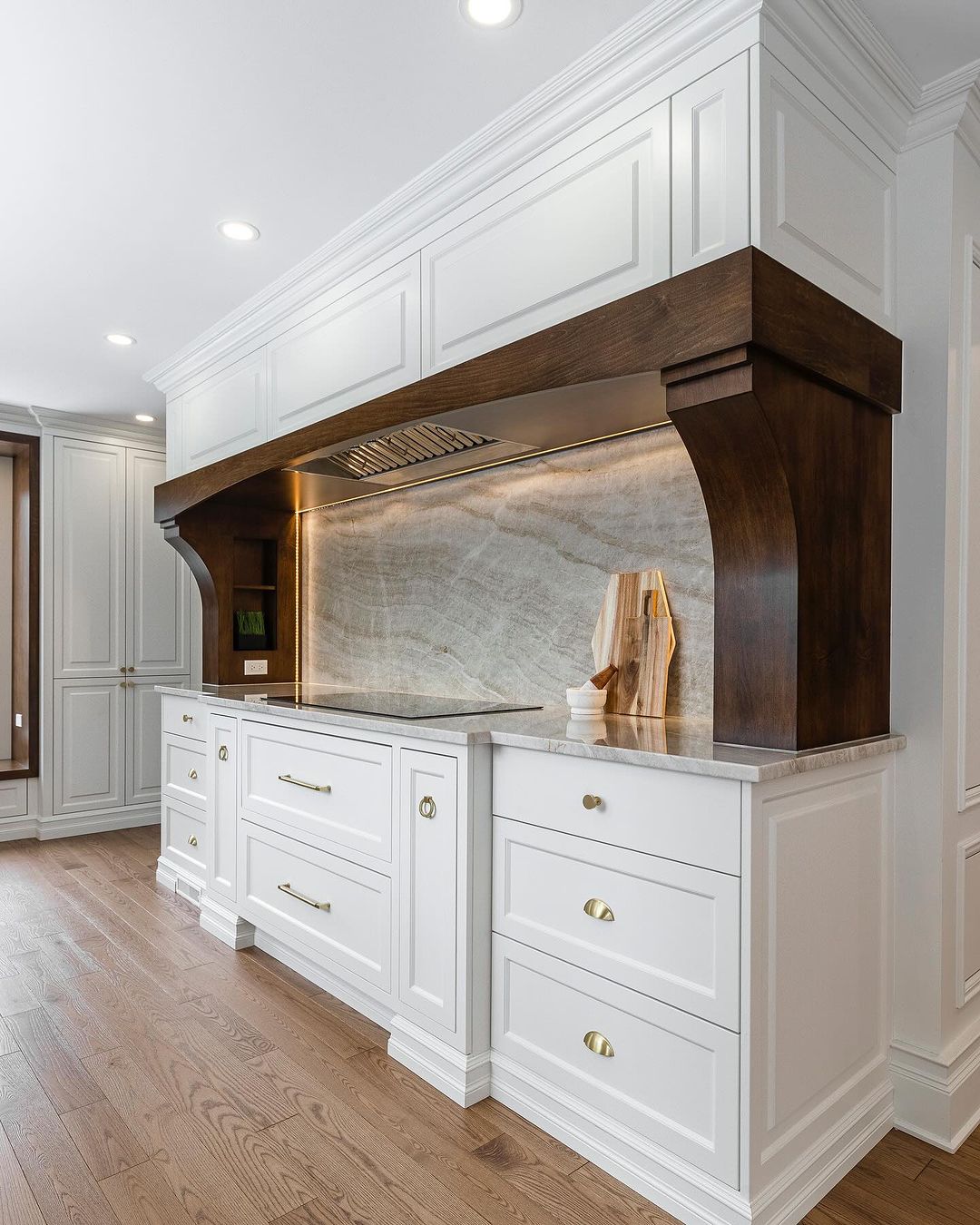Experience the perfect blend of modern elegance and traditional charm in this stunning kitchen featuring white cabinetry and a dark wood hood.