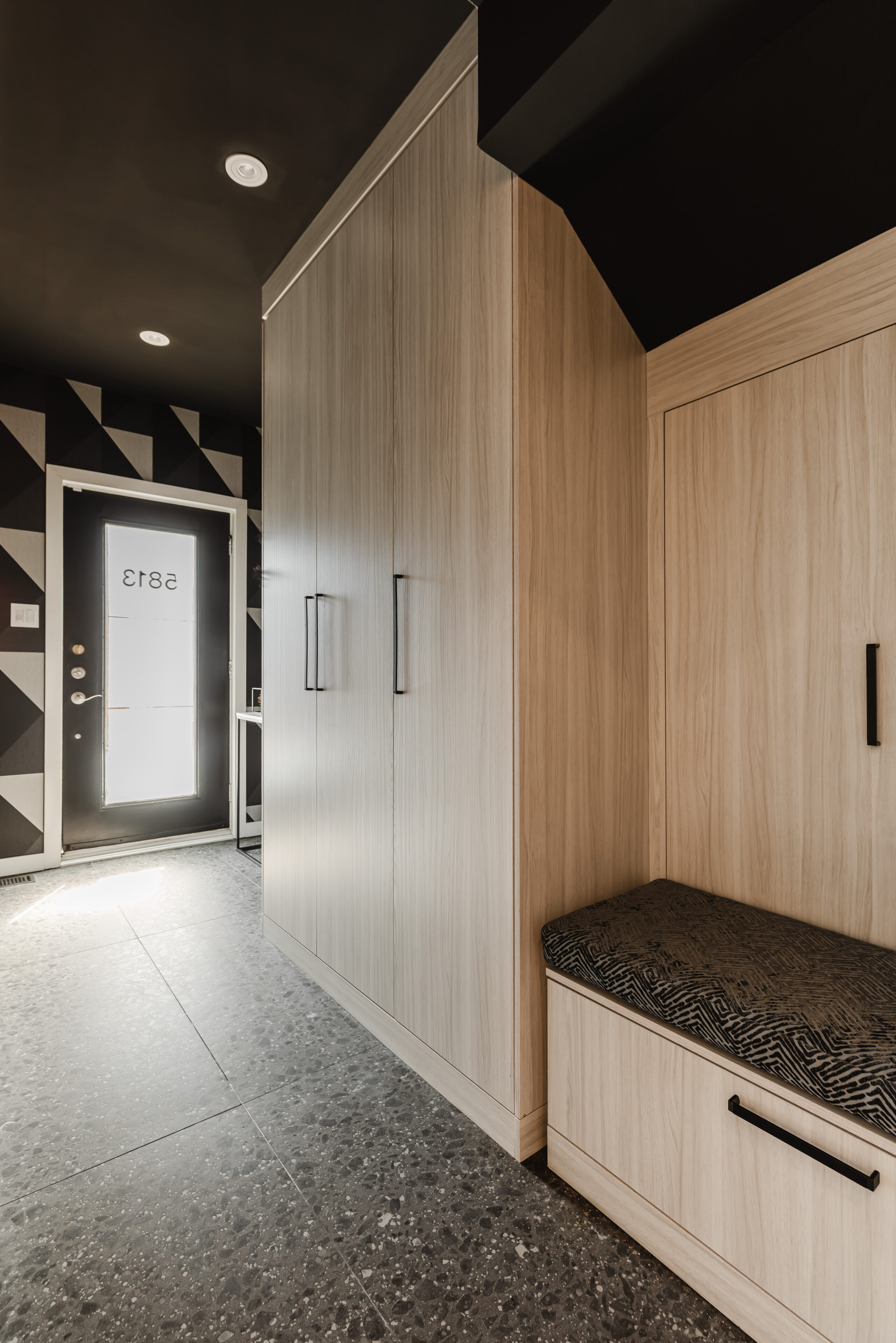 Stylish modern entryway featuring a light wood cabinet, dark bench, and striking black and white geometric wall design for a functional welcome.