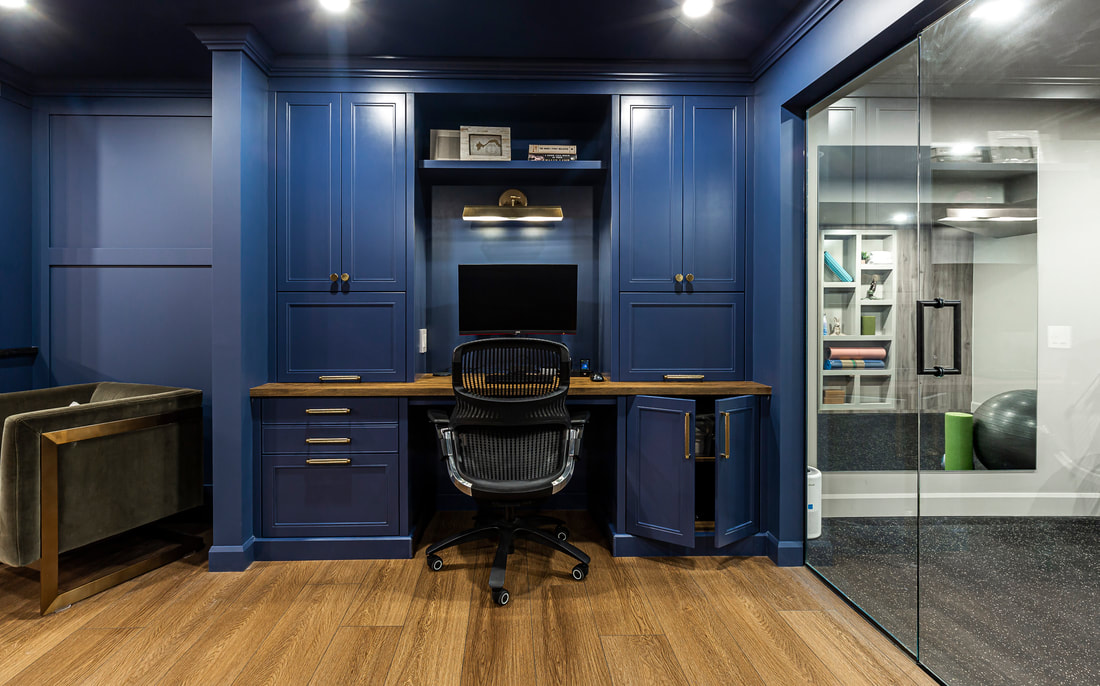 Elevate your workspace with this modern home office featuring deep blue walls, a sleek desk, and abundant natural light from a glass partition.
