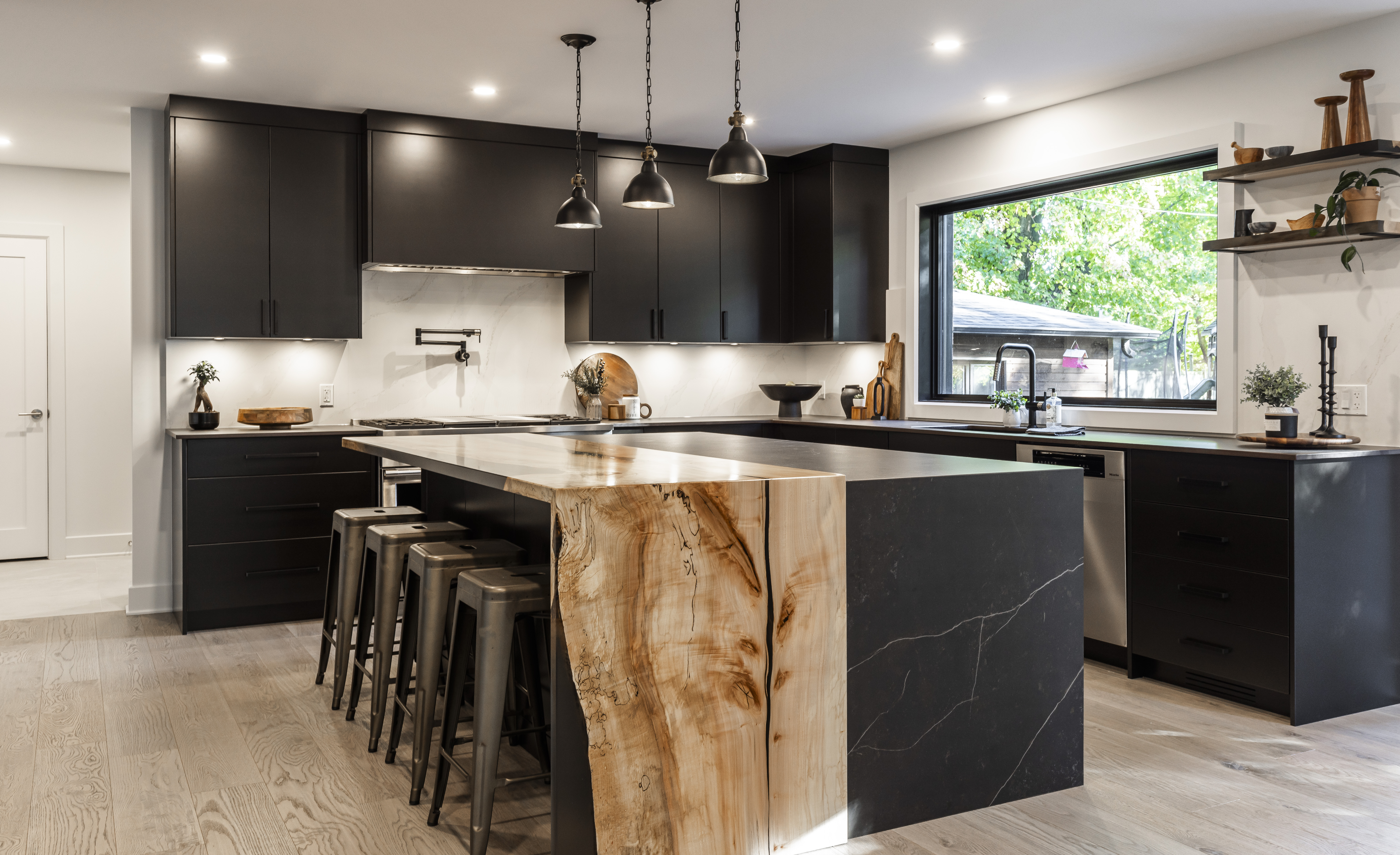Experience a stylish modern kitchen with sleek black cabinetry, a stunning stone island, and inviting warm lighting for cooking and socializing.