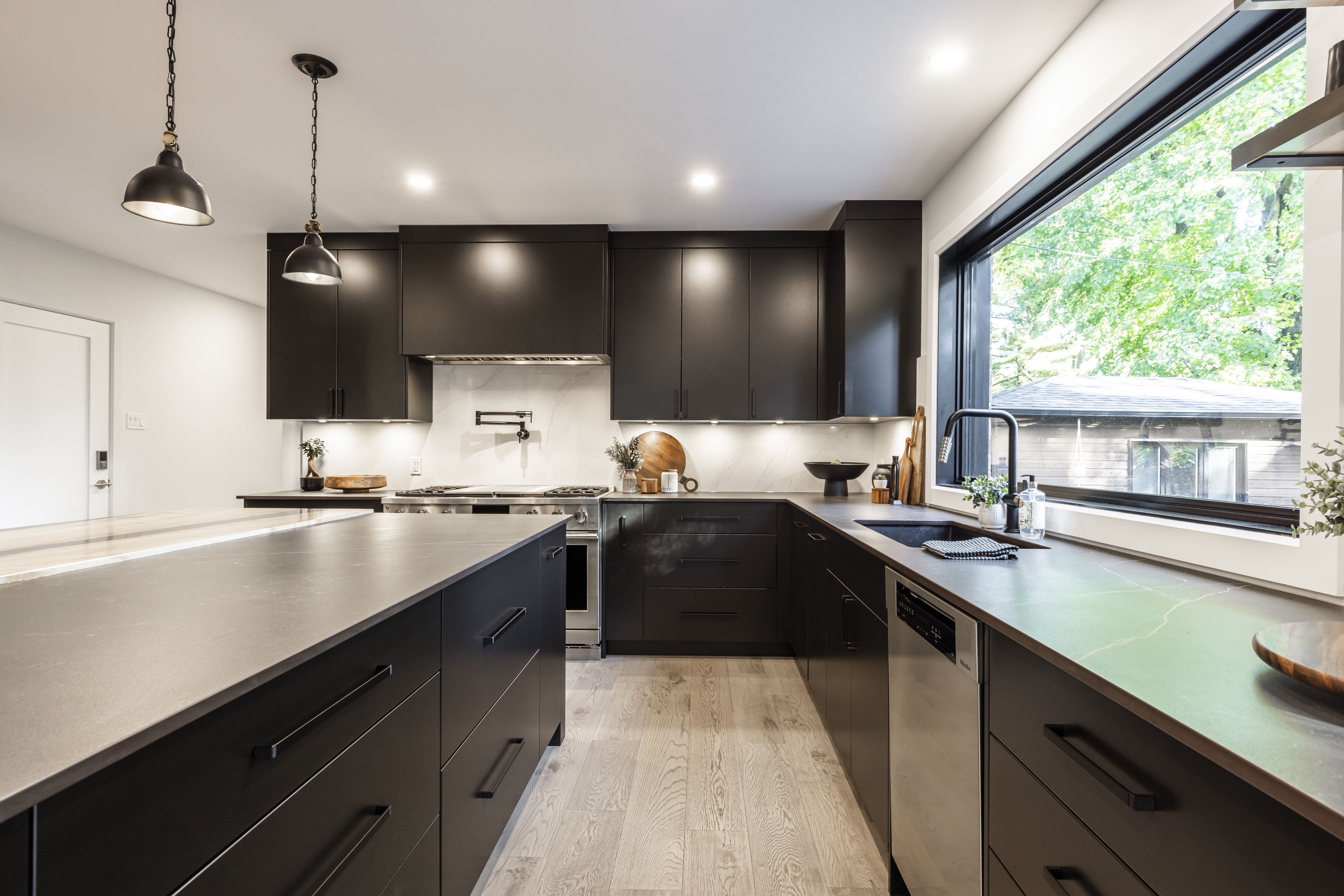 Stylish modern kitchen featuring sleek black cabinetry, a spacious island, and abundant natural light from a large window.