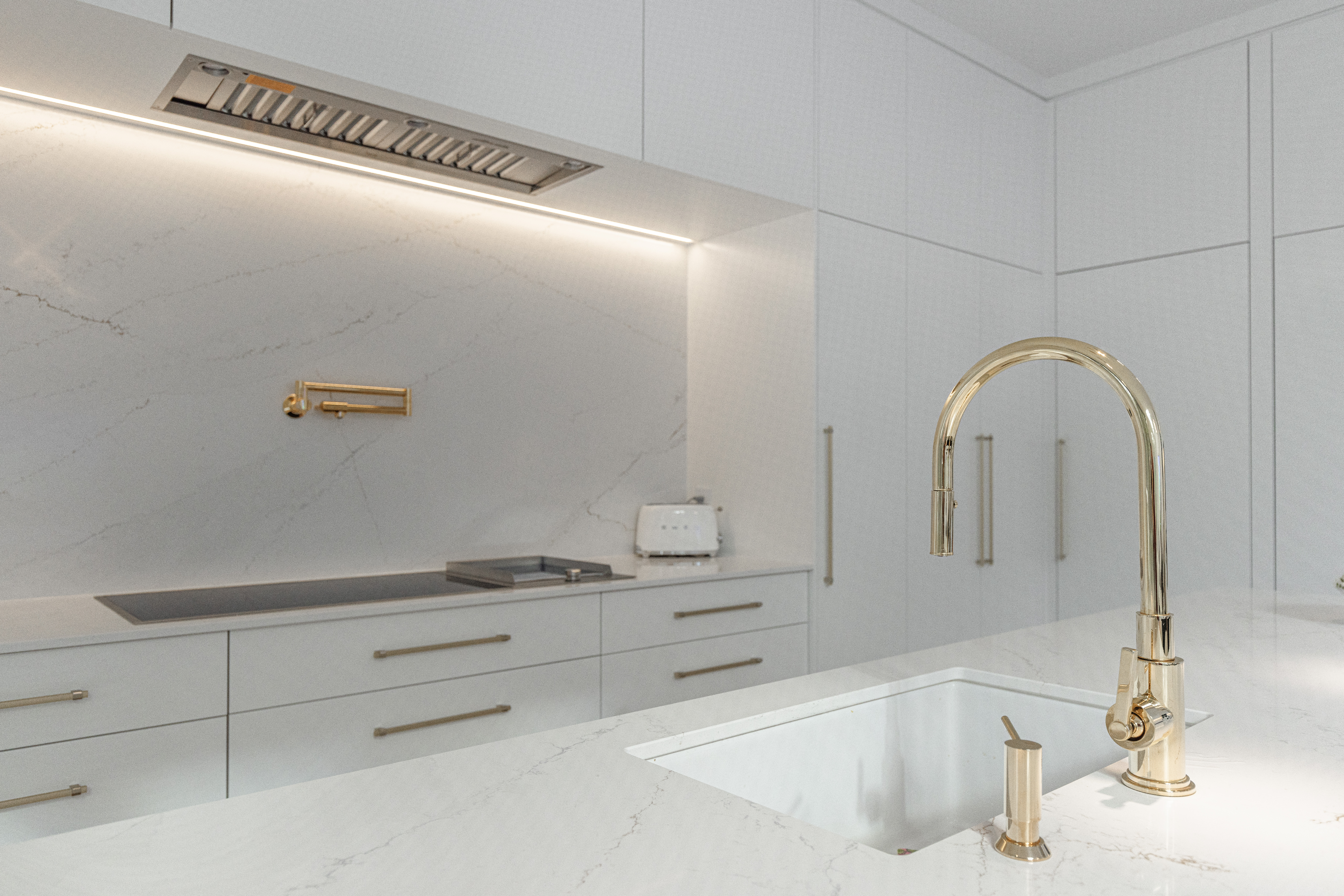 Stylish modern kitchen featuring light cabinetry, a gold faucet, and ambient lighting for a chic and functional space.
