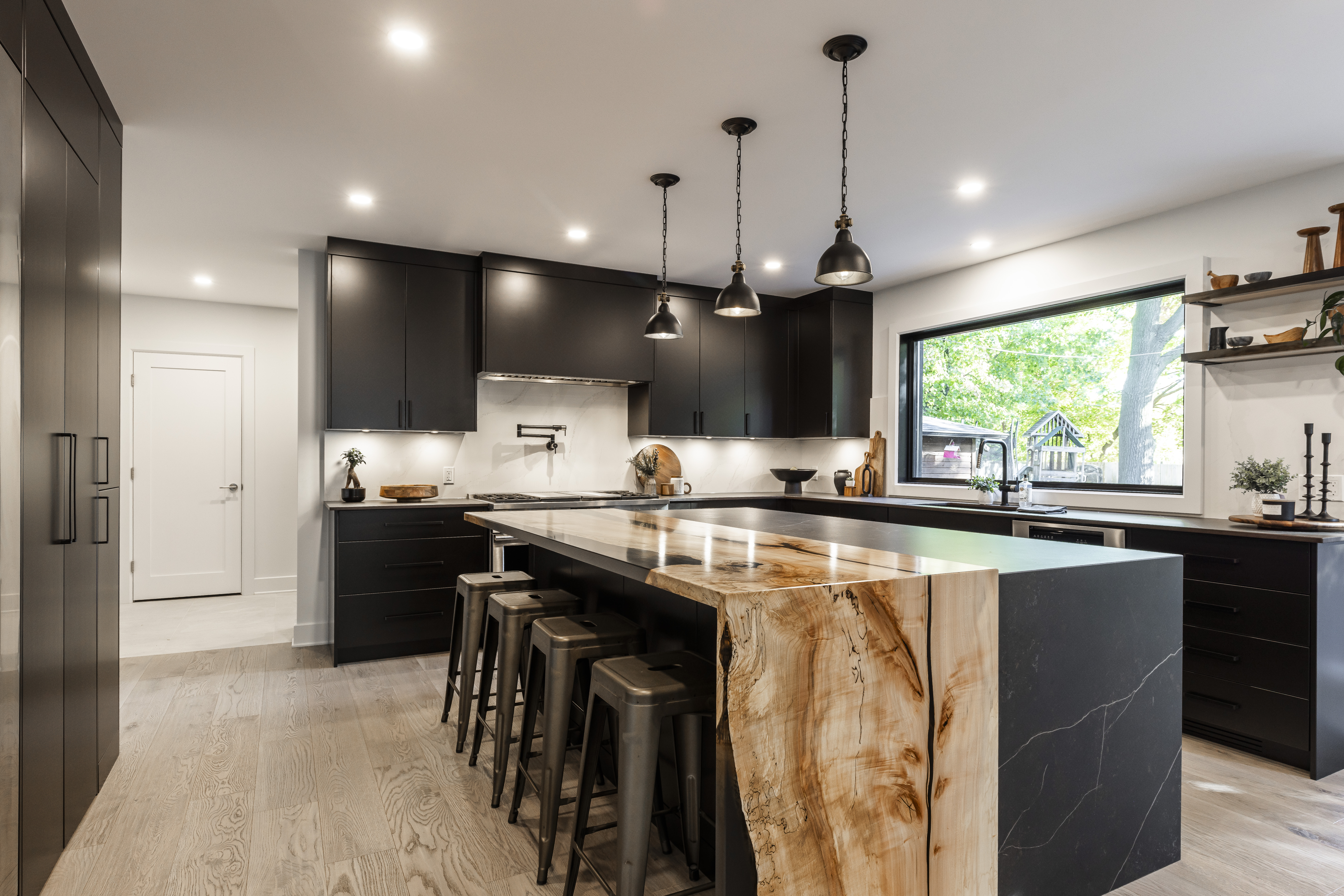 Experience modern elegance with a sleek black kitchen, a striking stone island, and welcoming natural light enhancing the stylish decor.