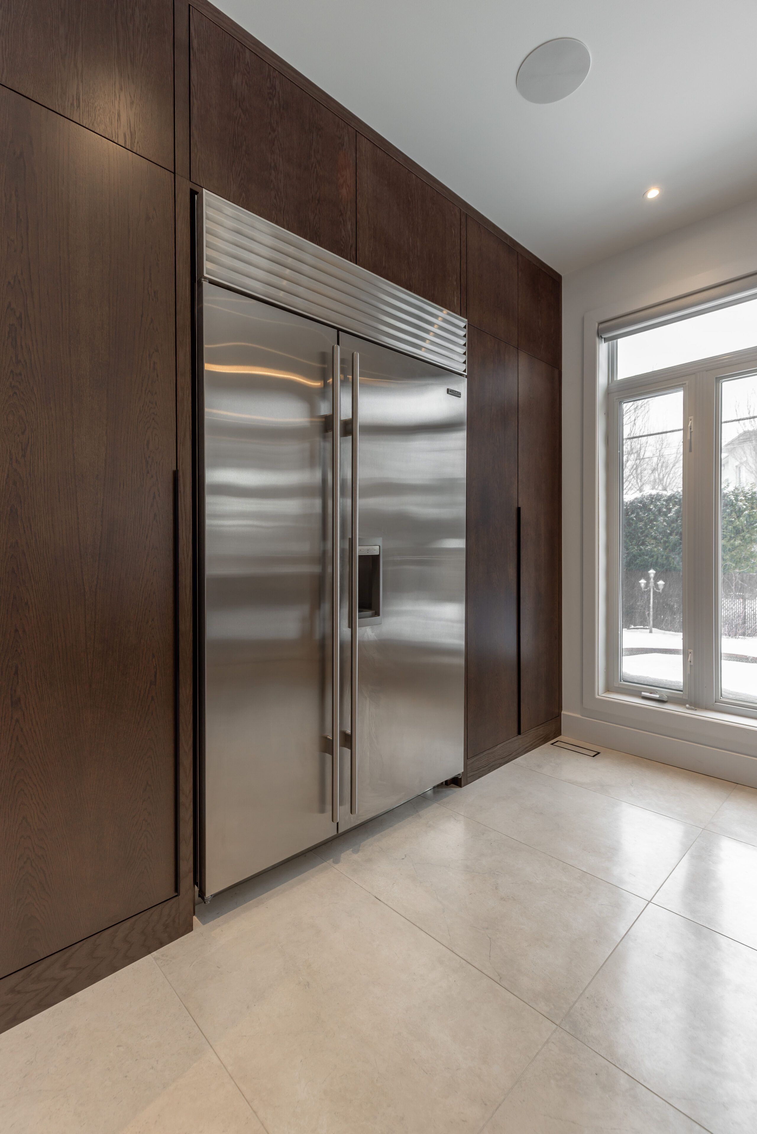 Modern kitchen featuring a sleek stainless steel refrigerator, dark cabinetry, and abundant natural light for a bright and inviting atmosphere.
