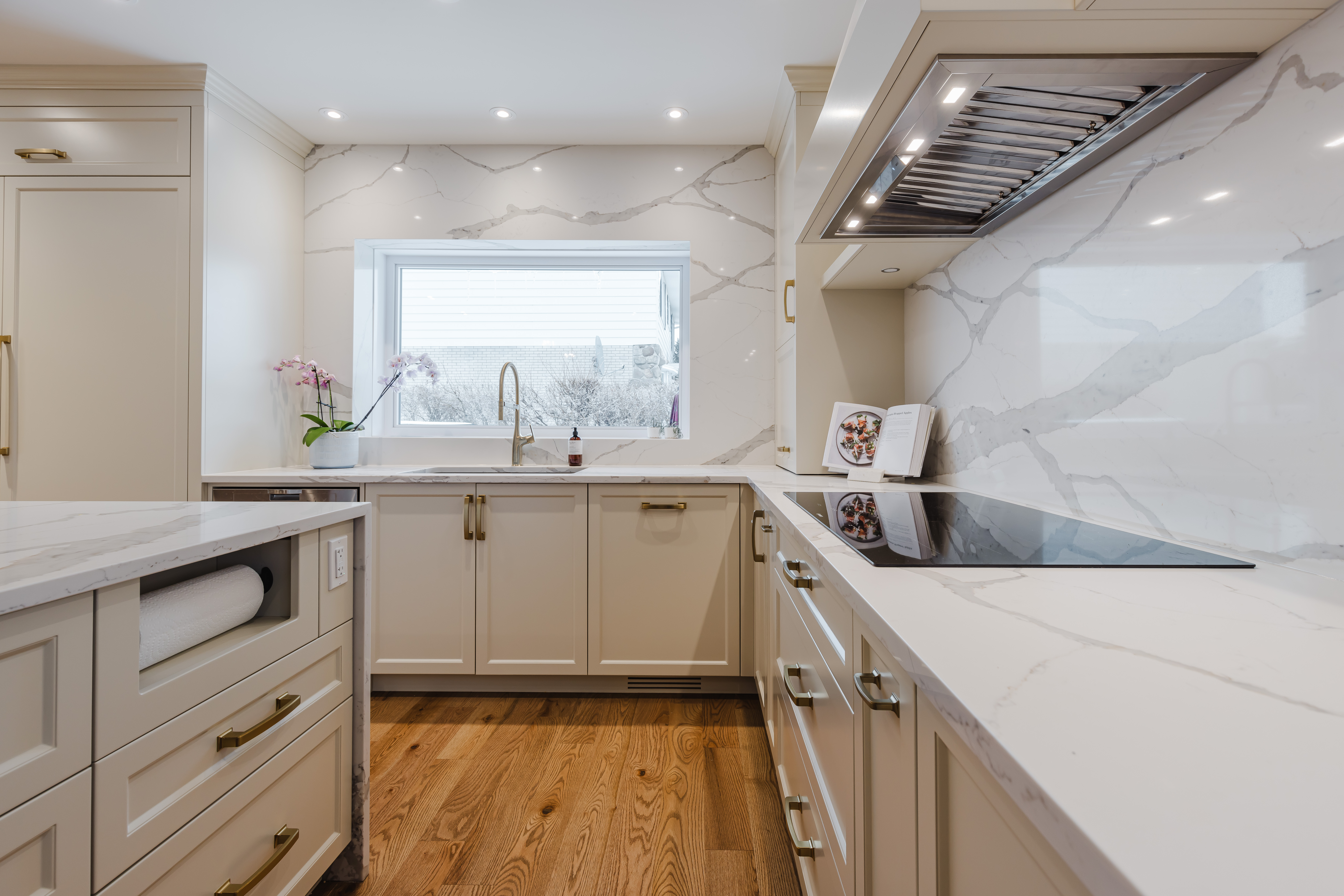 Bright and elegant modern kitchen featuring cream cabinetry, a sleek island, and natural light enhancing the warm hardwood floors.
