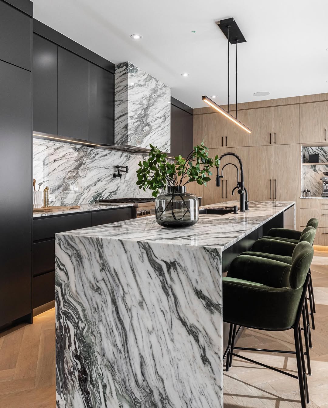 Sophisticated modern kitchen featuring a marble island, sleek black cabinets, and inviting deep green bar stools for a stylish gathering space.