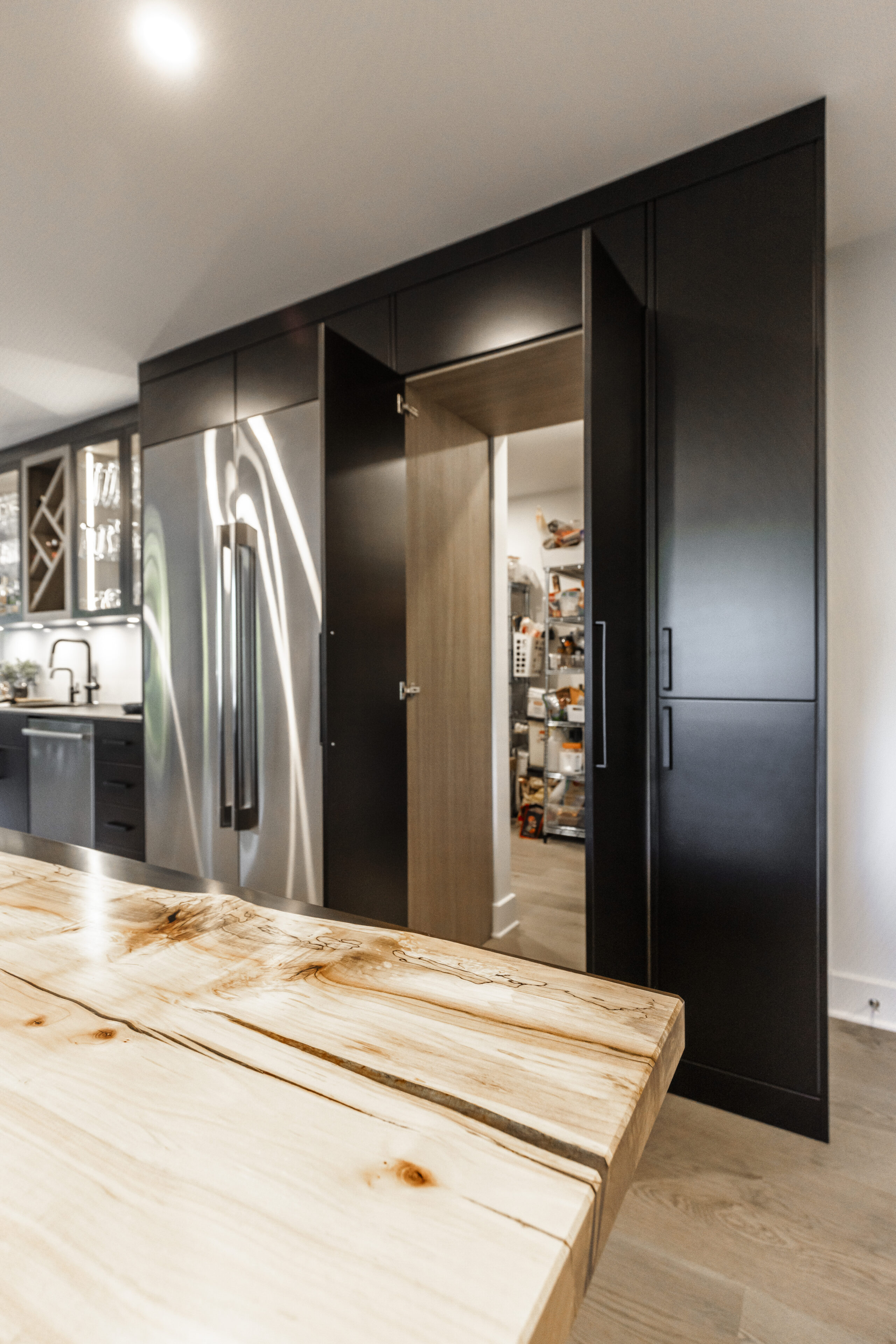 A sleek modern kitchen features black cabinetry, stainless steel appliances, and a warm rustic wooden table for inviting dining experiences.