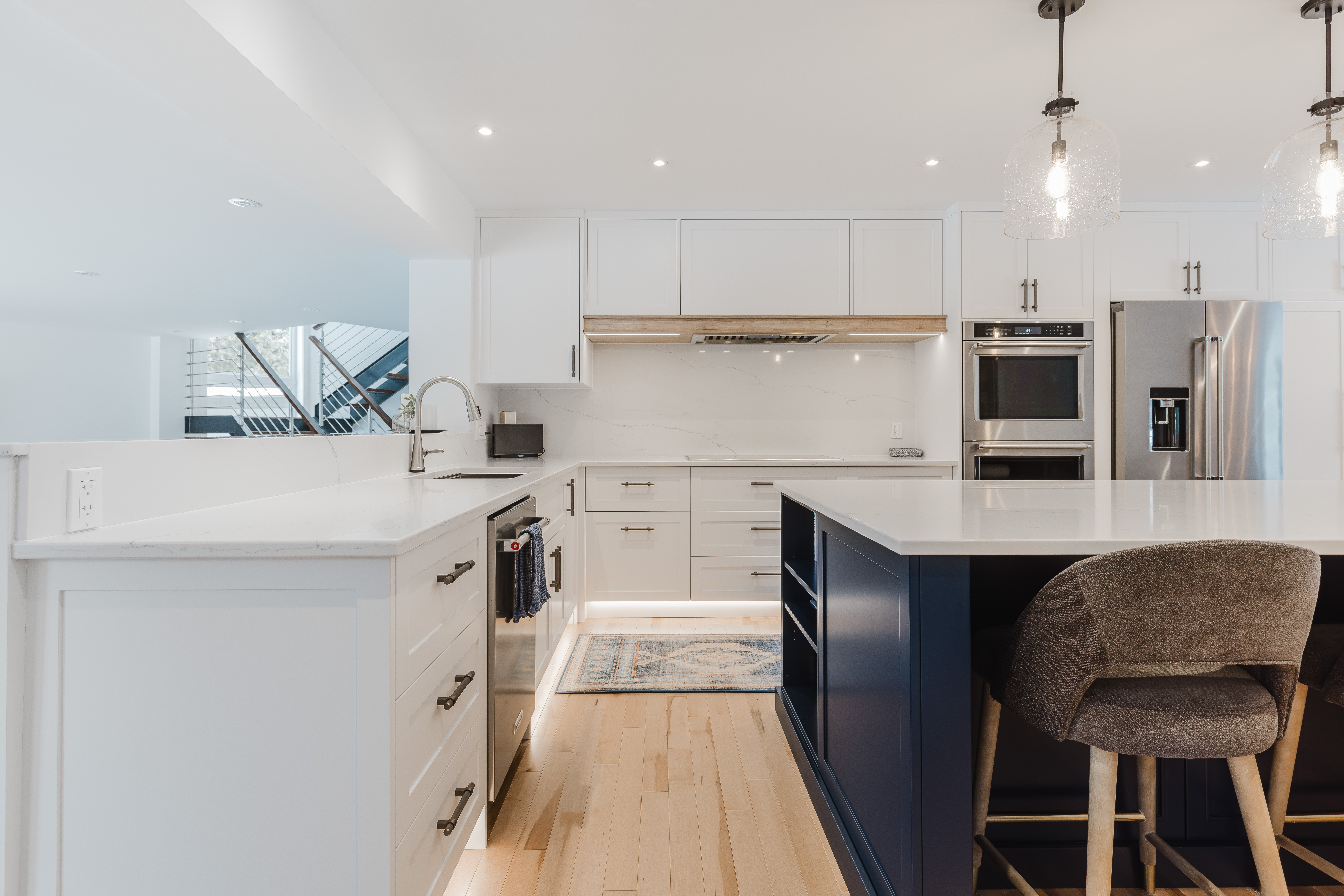 Experience modern elegance in this inviting kitchen featuring a stunning white and navy island, warm wood flooring, and stylish lighting.