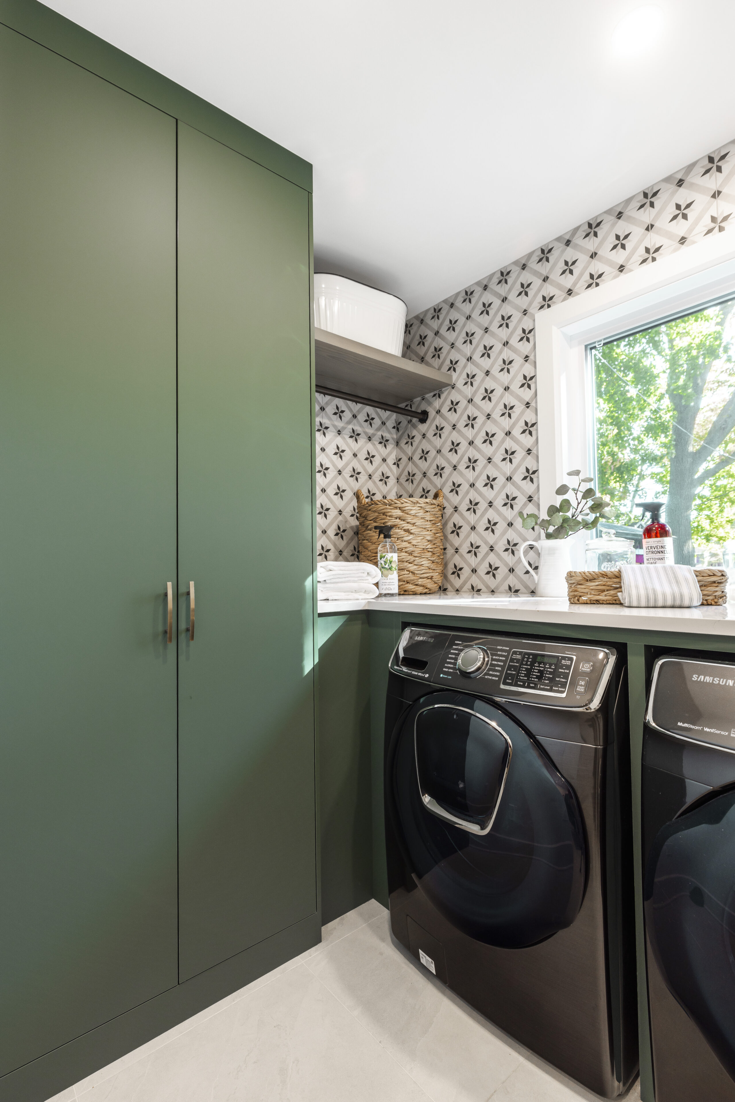 Modern laundry room featuring stylish green cabinets, black appliances, and natural light for an inviting and functional space.