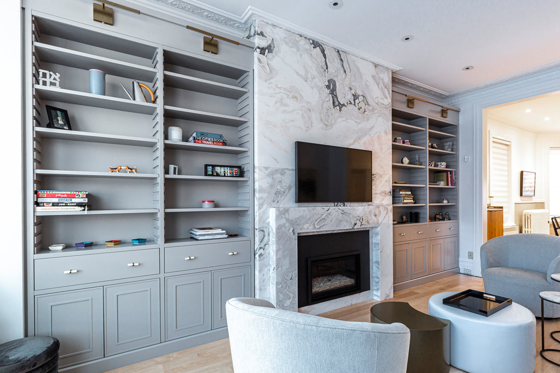 Modern living room featuring elegant gray shelving, a luxurious marbled wall with a flat-screen TV, and cozy seating bathed in natural light.