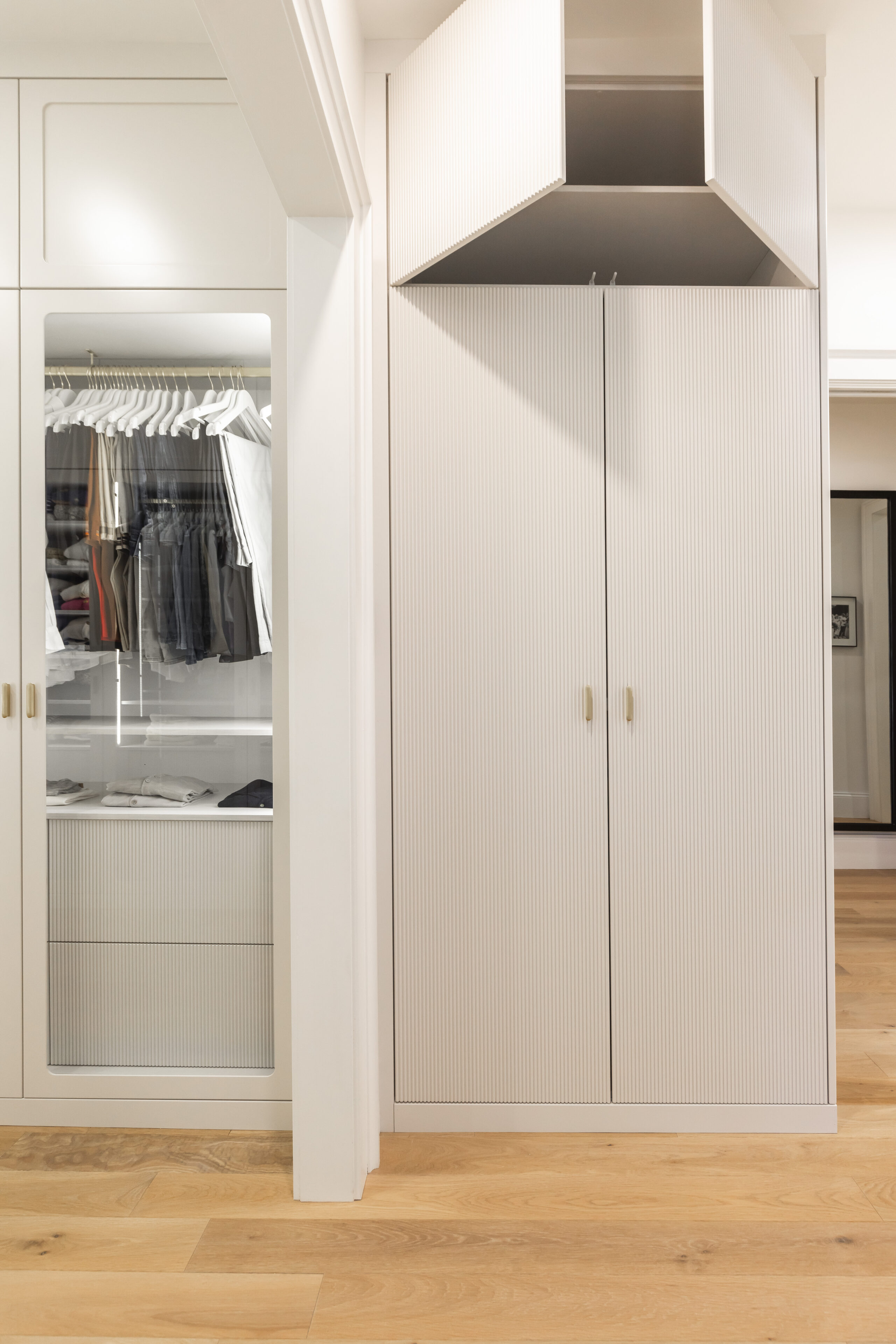 Discover a stylish modern closet featuring organized clothing, glass panels, and elegant gold accents on a warm wooden floor.