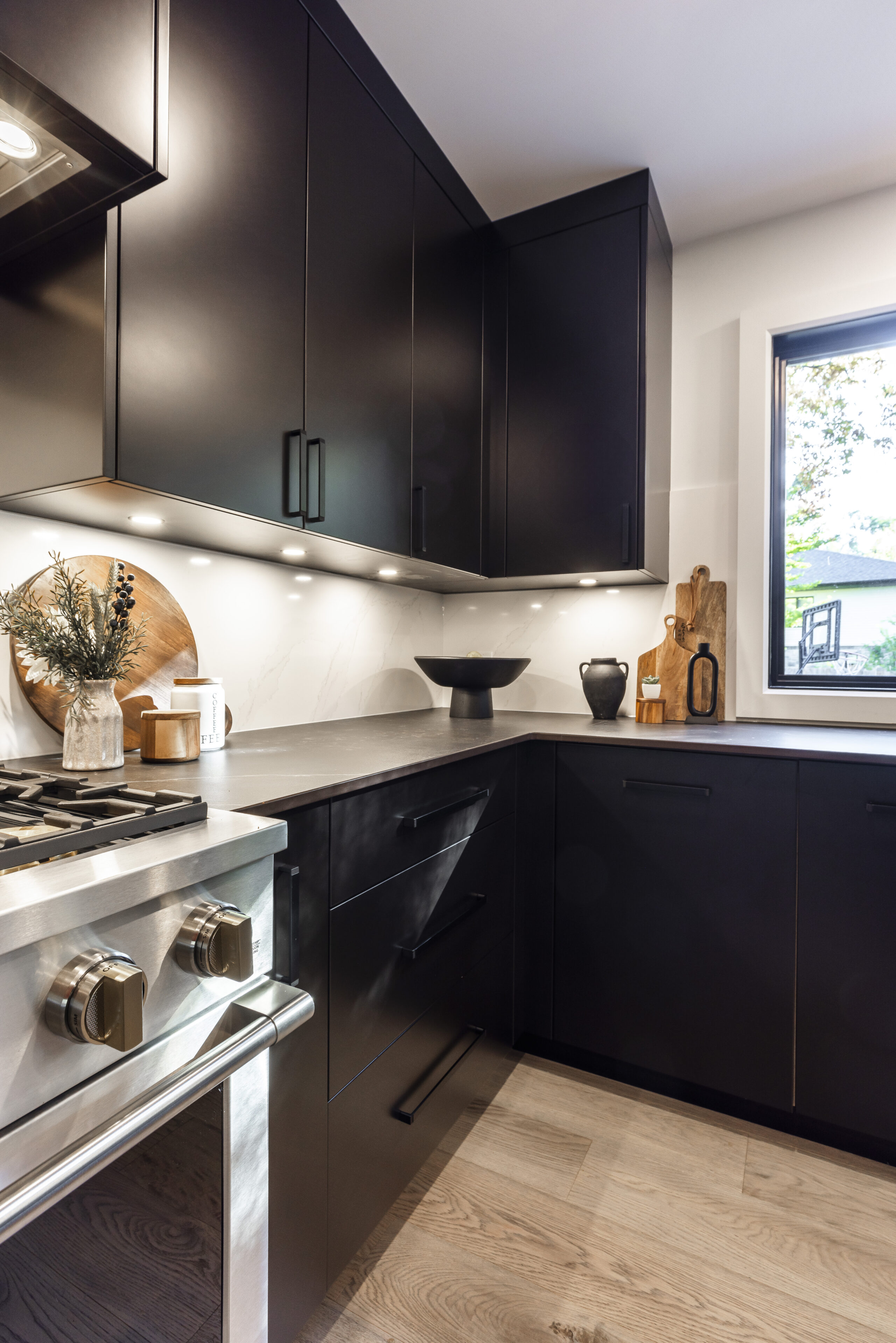 Experience the elegance of this modern minimalist kitchen with black cabinetry, light countertops, and a bright ambiance enhanced by natural light.