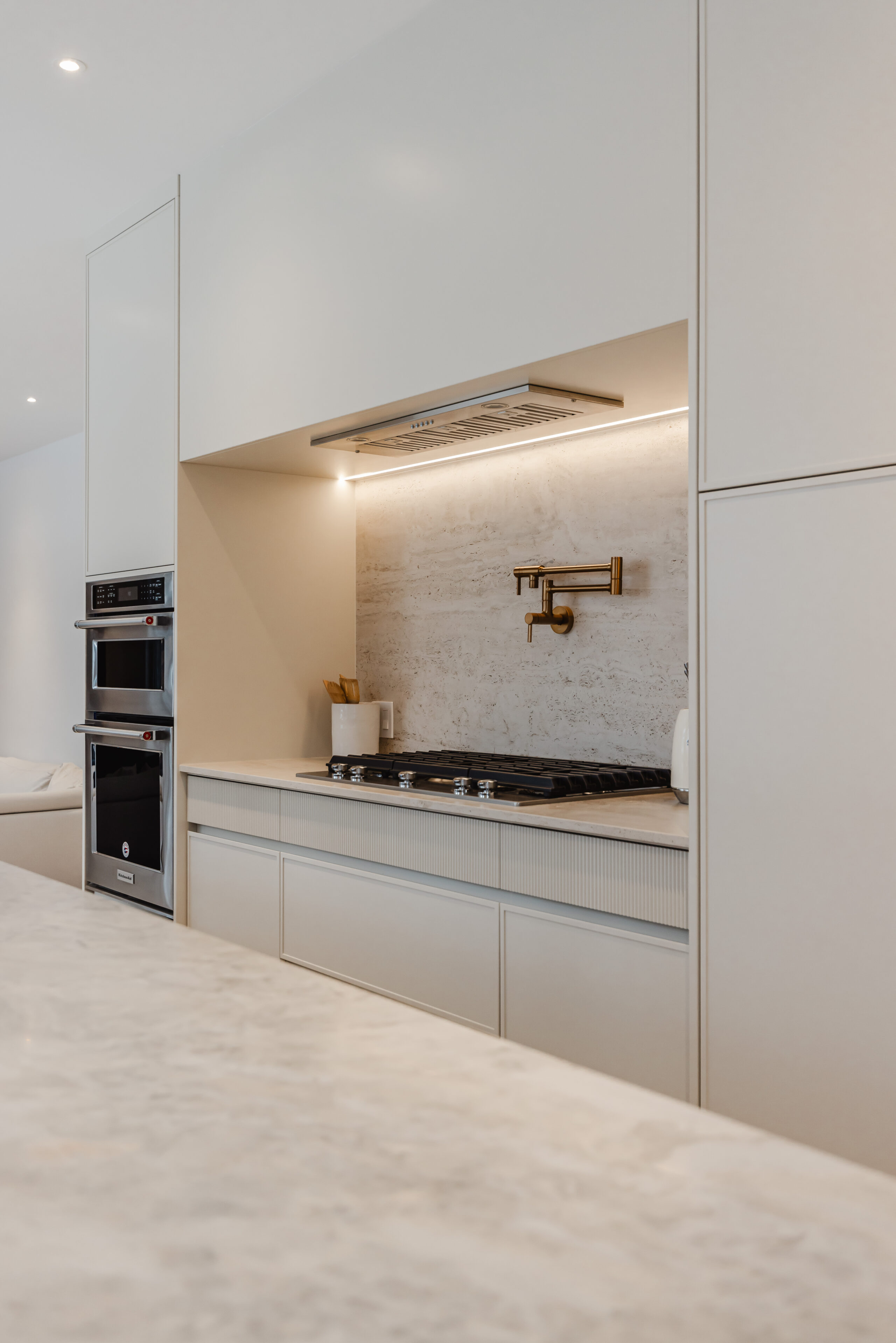 Experience a sophisticated modern kitchen with sleek white cabinetry, stainless steel appliances, and inviting under-cabinet lighting for stylish gatherings.