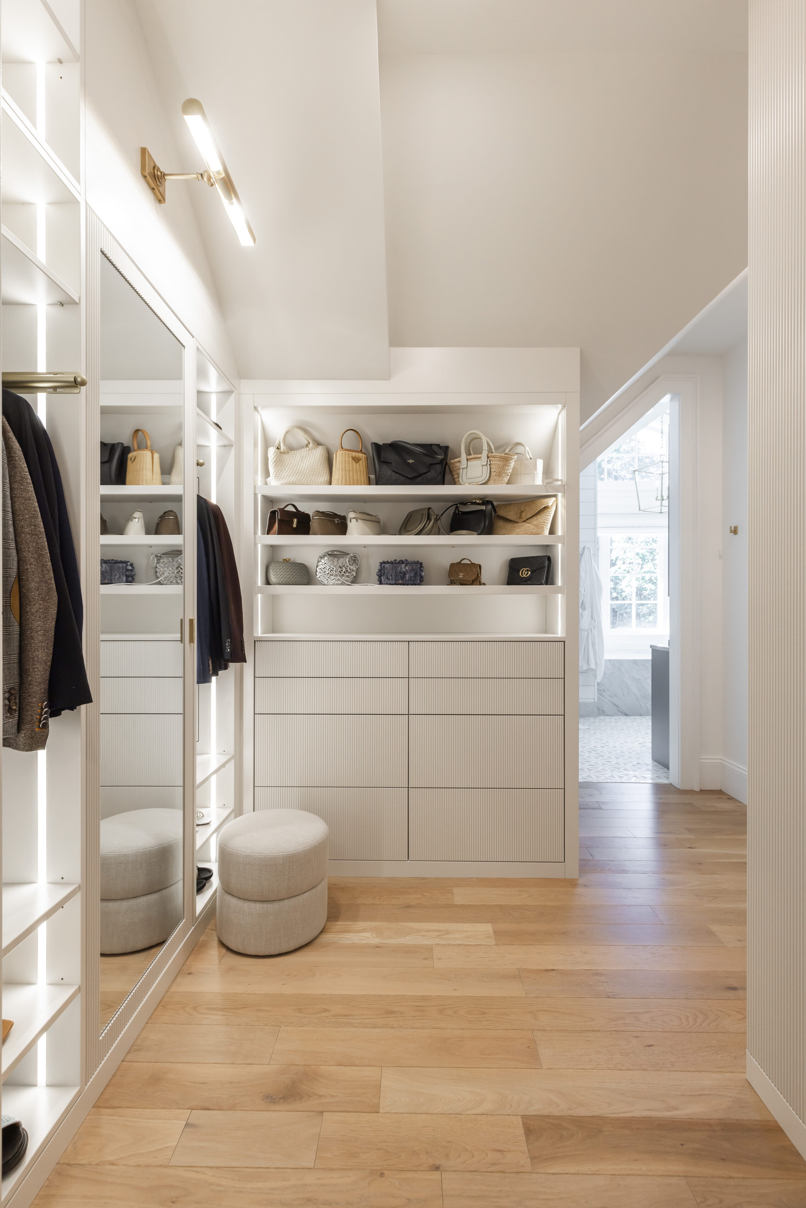 Discover a stylish modern closet featuring sleek white cabinetry, organized storage, cozy seating, and abundant natural light.