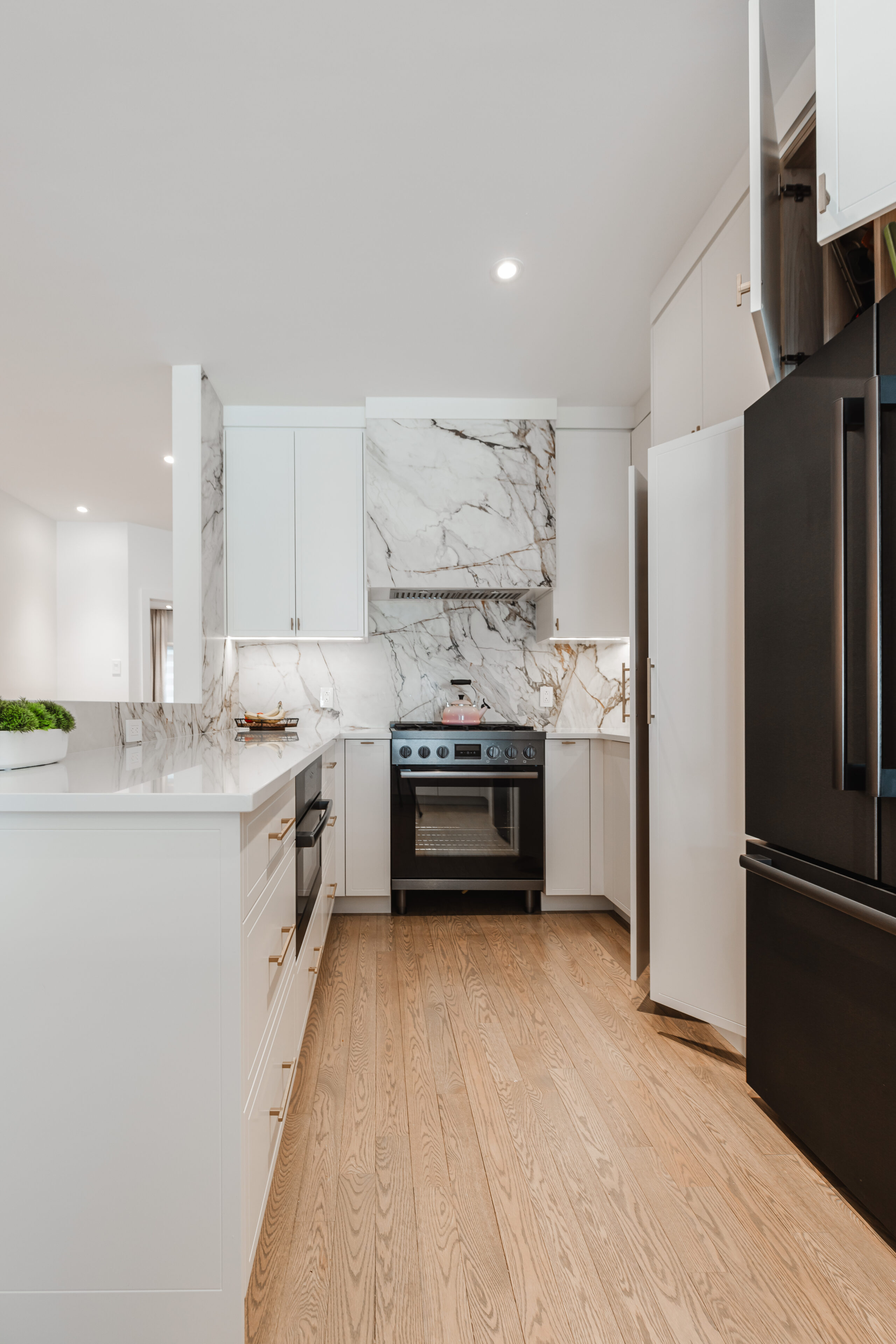 Sleek white kitchen with elegant marble backsplash, contrasting dark appliances, and warm wood flooring creates a stylish and inviting cooking space.