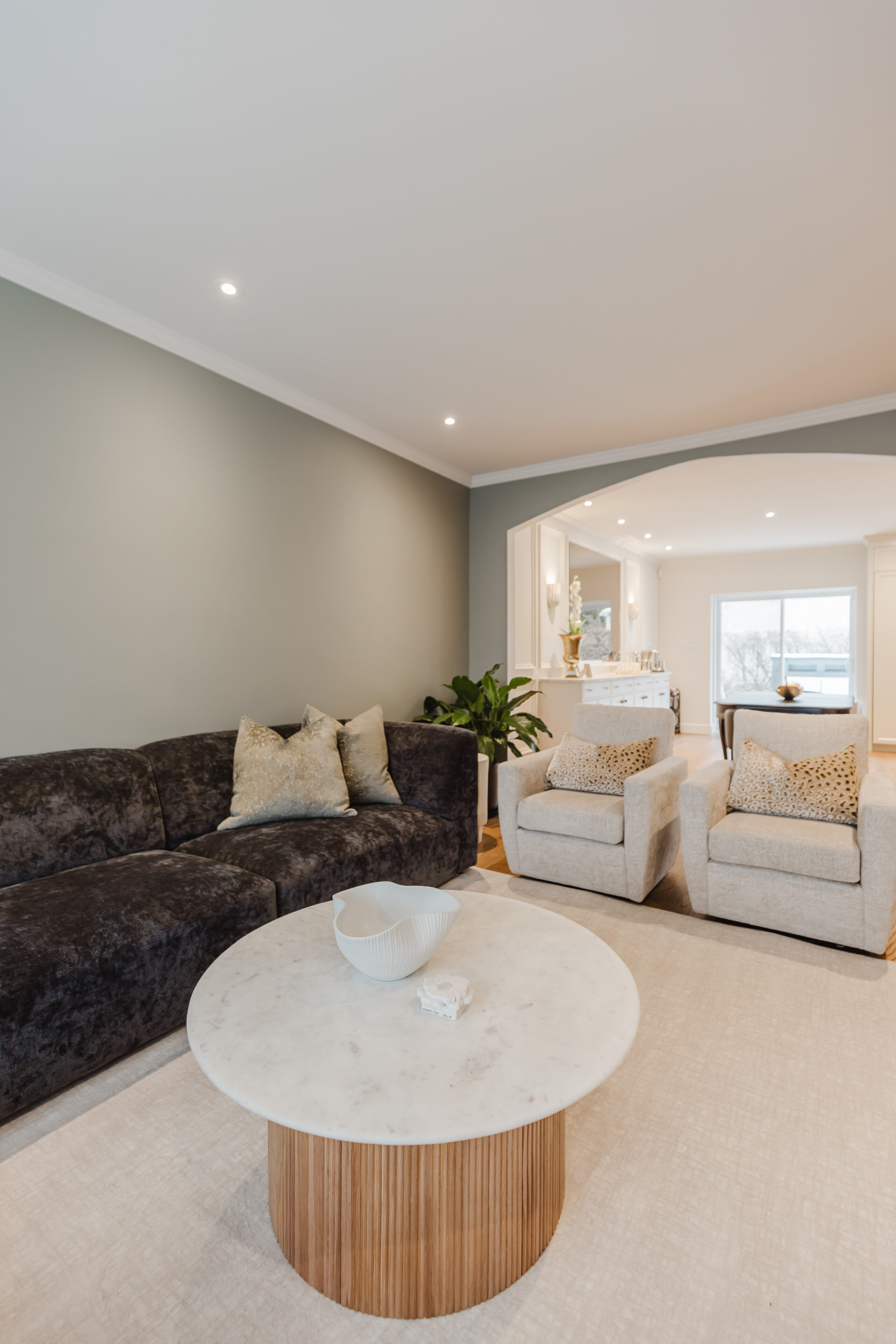 Cozy and elegant, this modern living room features a dark sectional sofa, a round coffee table, and inviting armchairs for stylish comfort.
