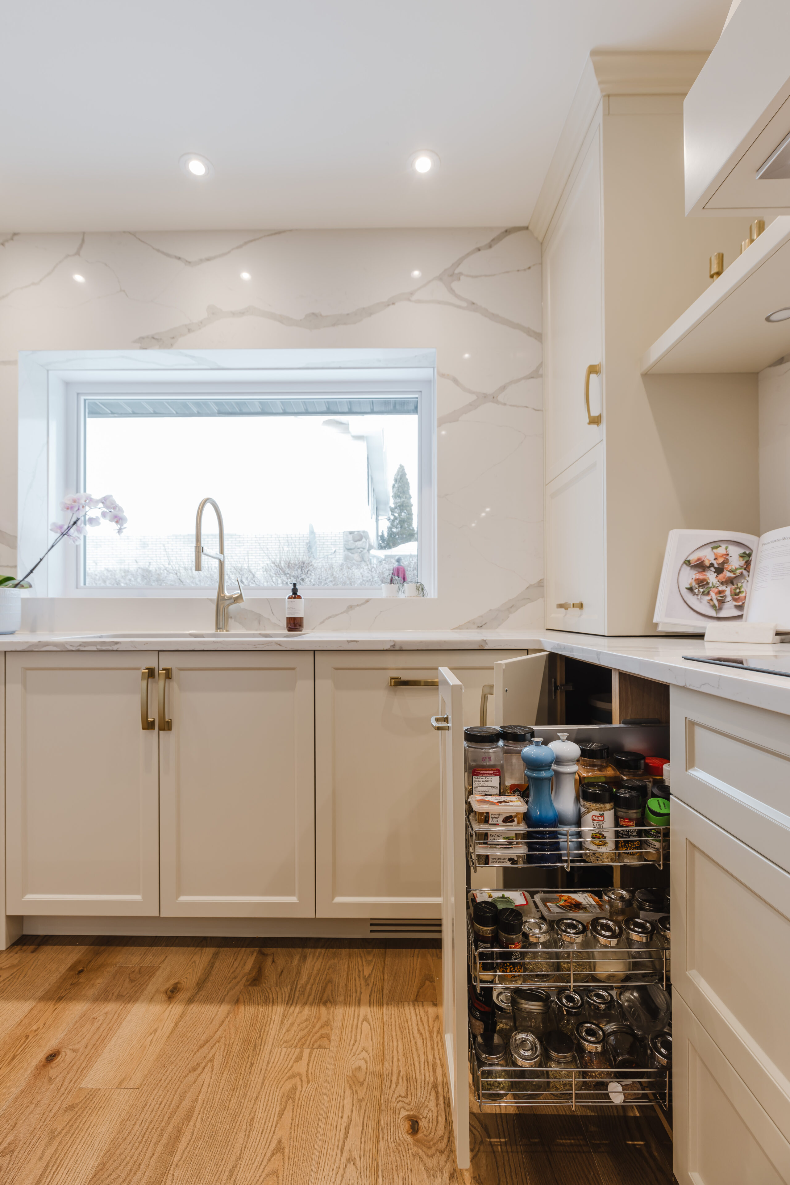 A stunning modern white kitchen features gold accents, a marble countertop, and abundant natural light, creating an inviting cooking space.