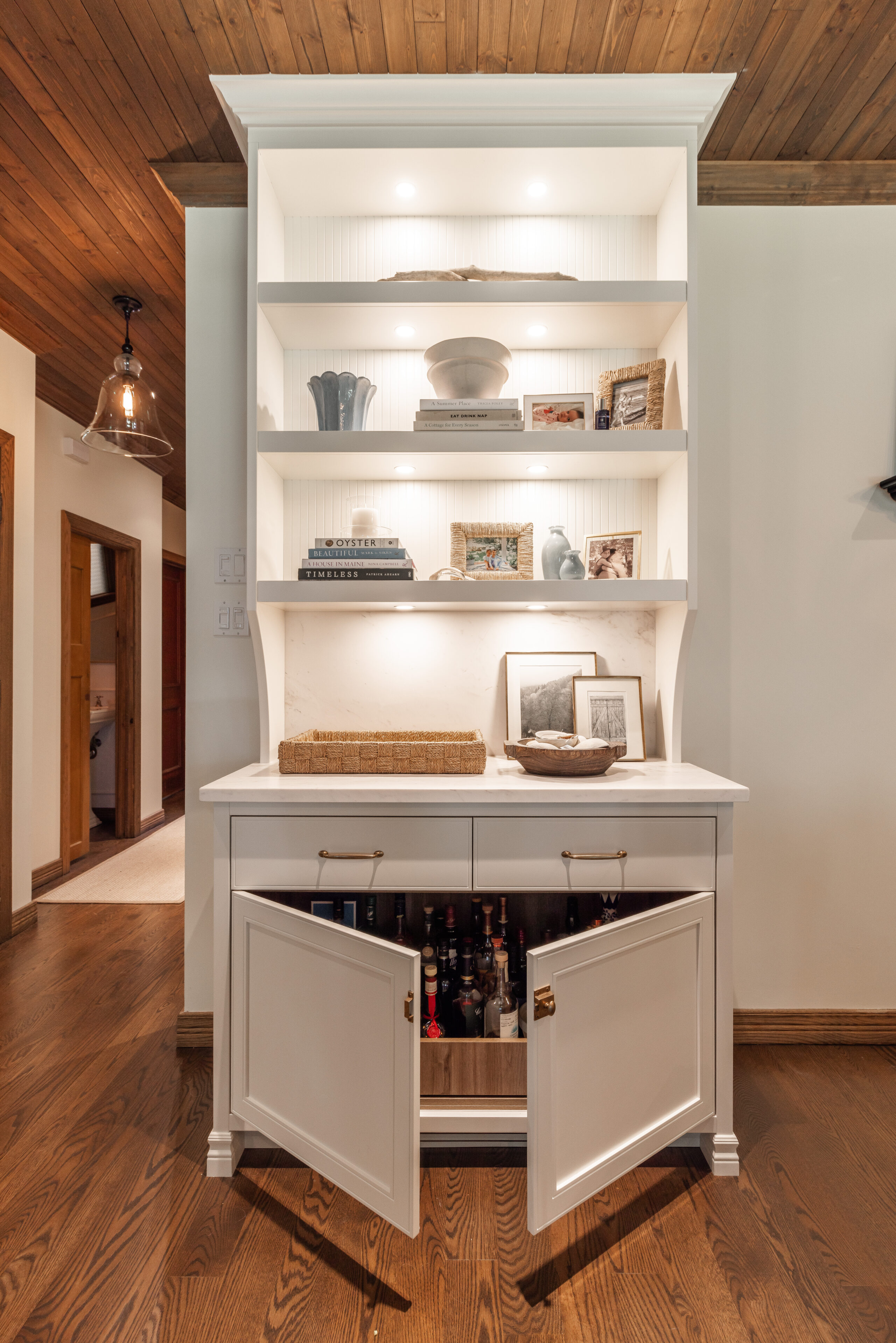 A chic white shelving unit displays decorative items and wine storage, enhancing a warm and inviting interior space.