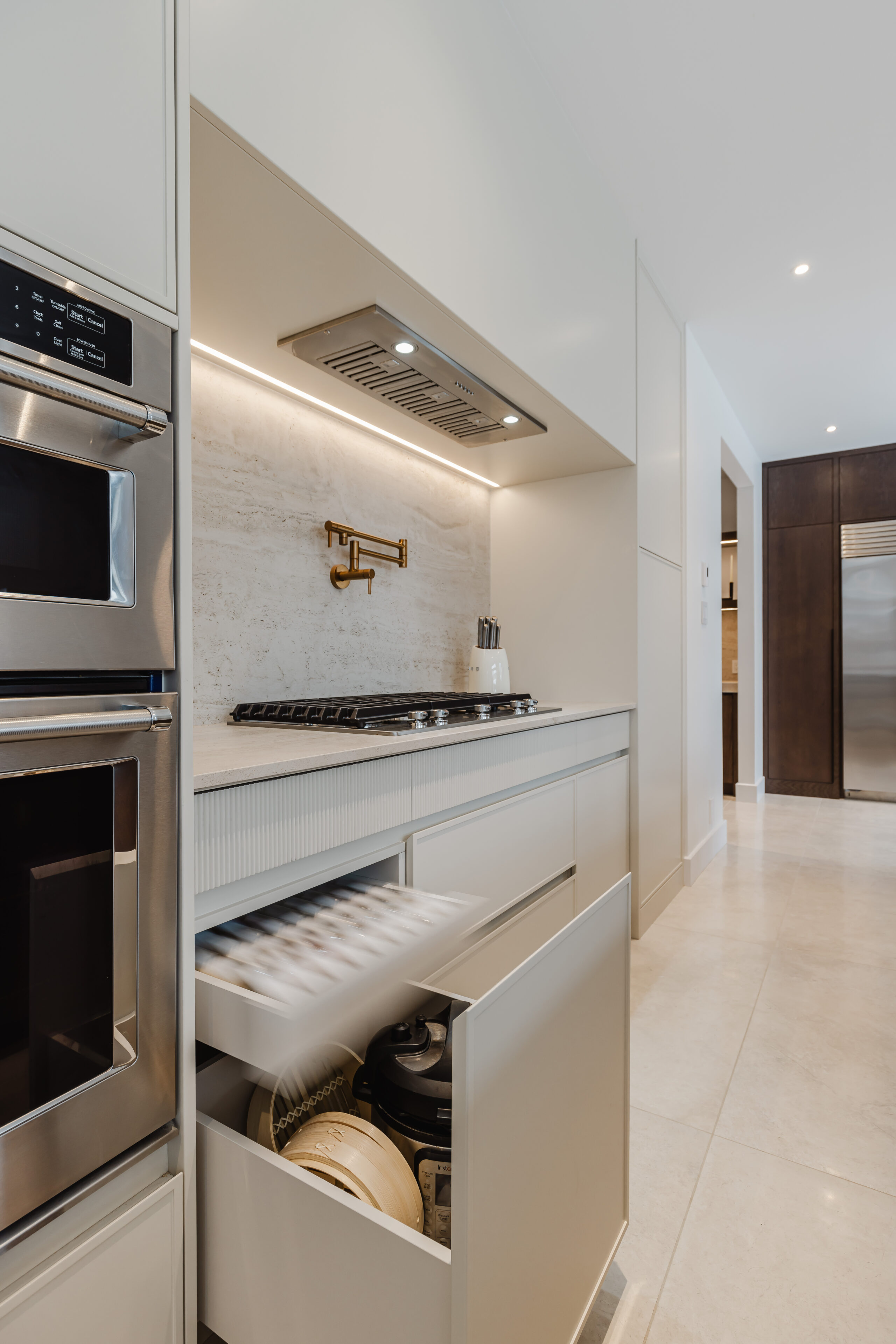 Discover a chic minimalist kitchen featuring neutral cabinetry, a central gas cooktop, and integrated stainless steel appliances for a sleek, modern design.