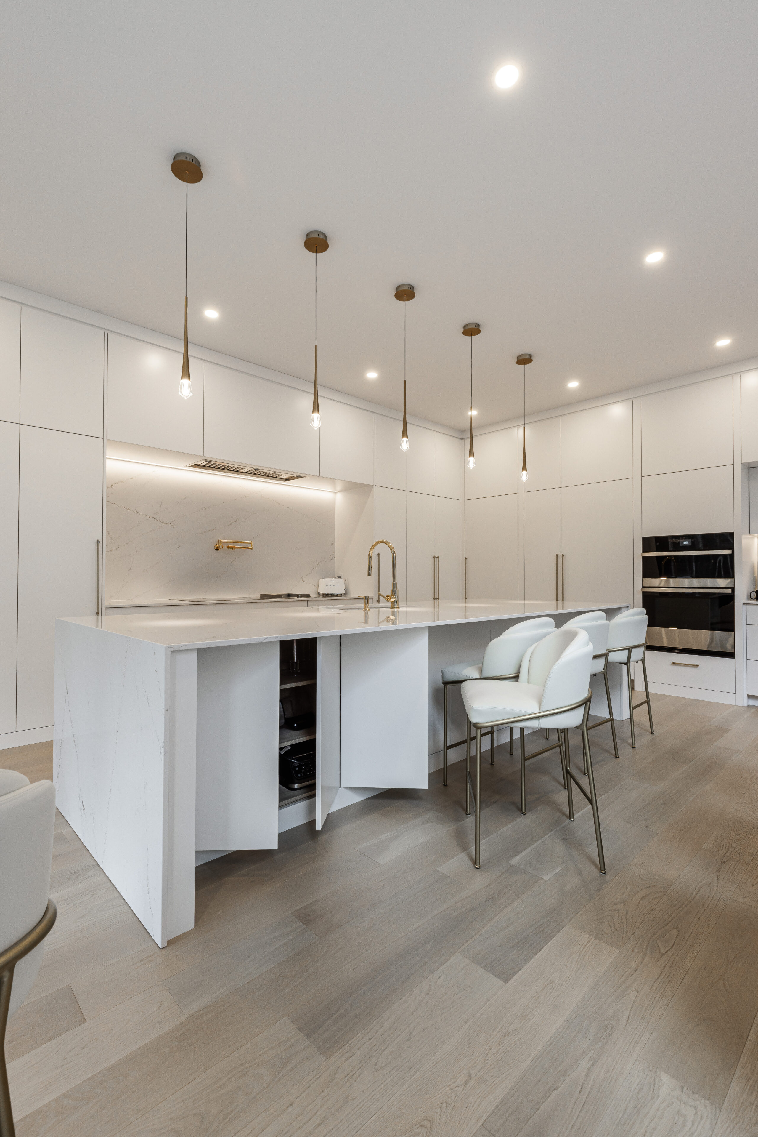 Discover a stylish minimalist white kitchen with a central island, elegant barstools, and seamless built-in appliances for a chic and inviting space.