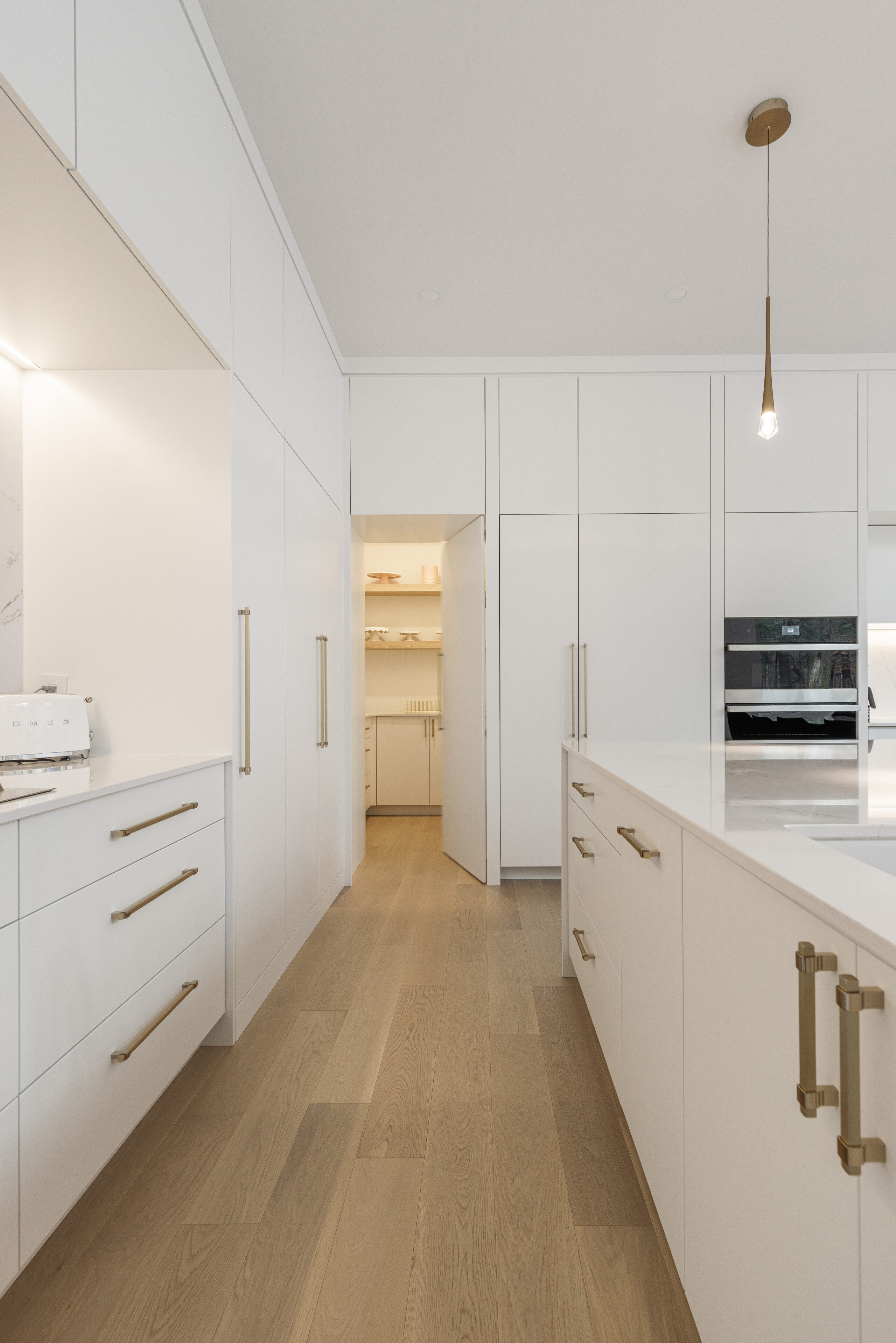 Stunning modern white kitchen featuring elegant golden accents, a spacious island, and seamless storage for a sophisticated, inviting atmosphere.
