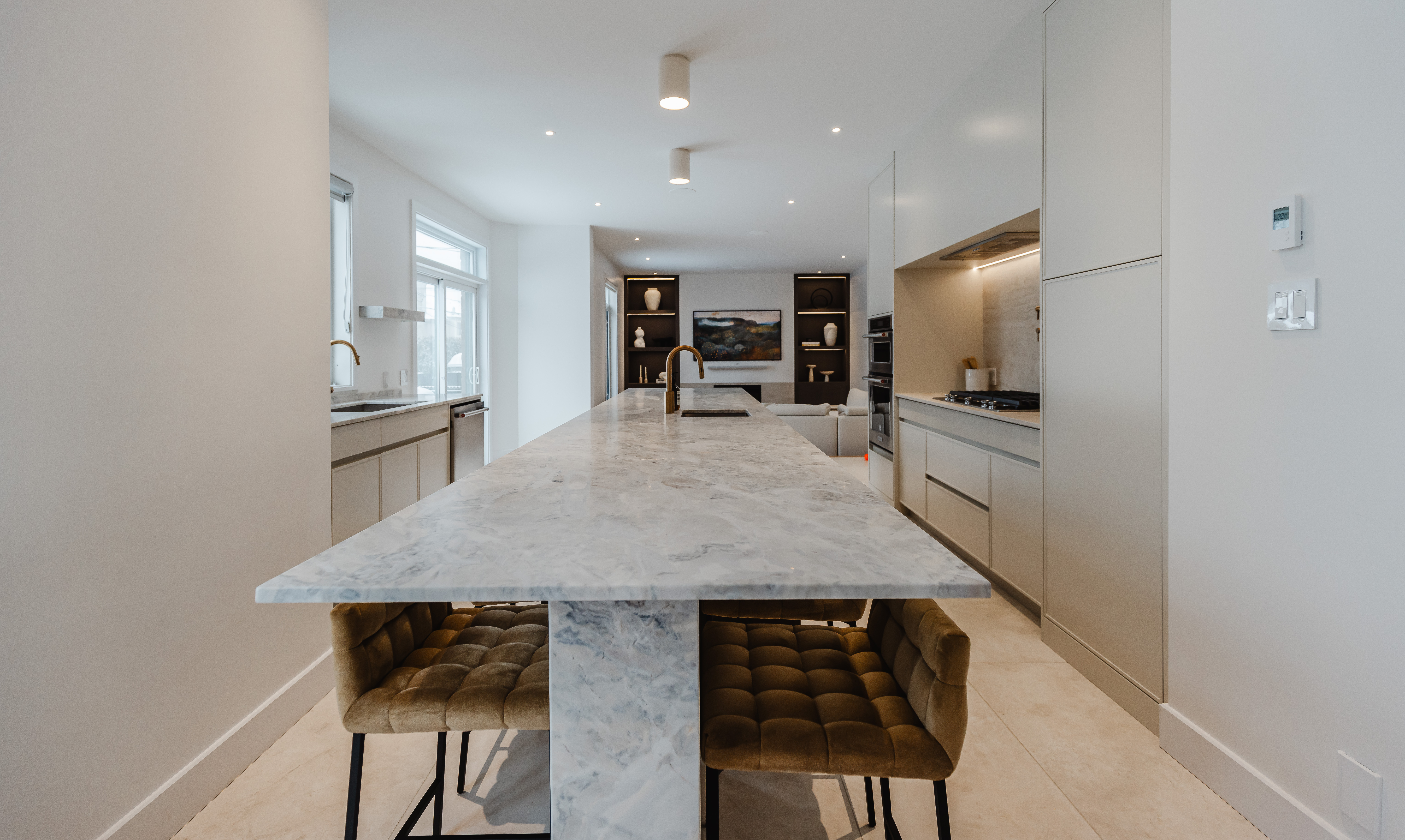 Discover a stunning modern kitchen featuring a marble island and cozy tufted stools, perfect for cooking and entertaining.