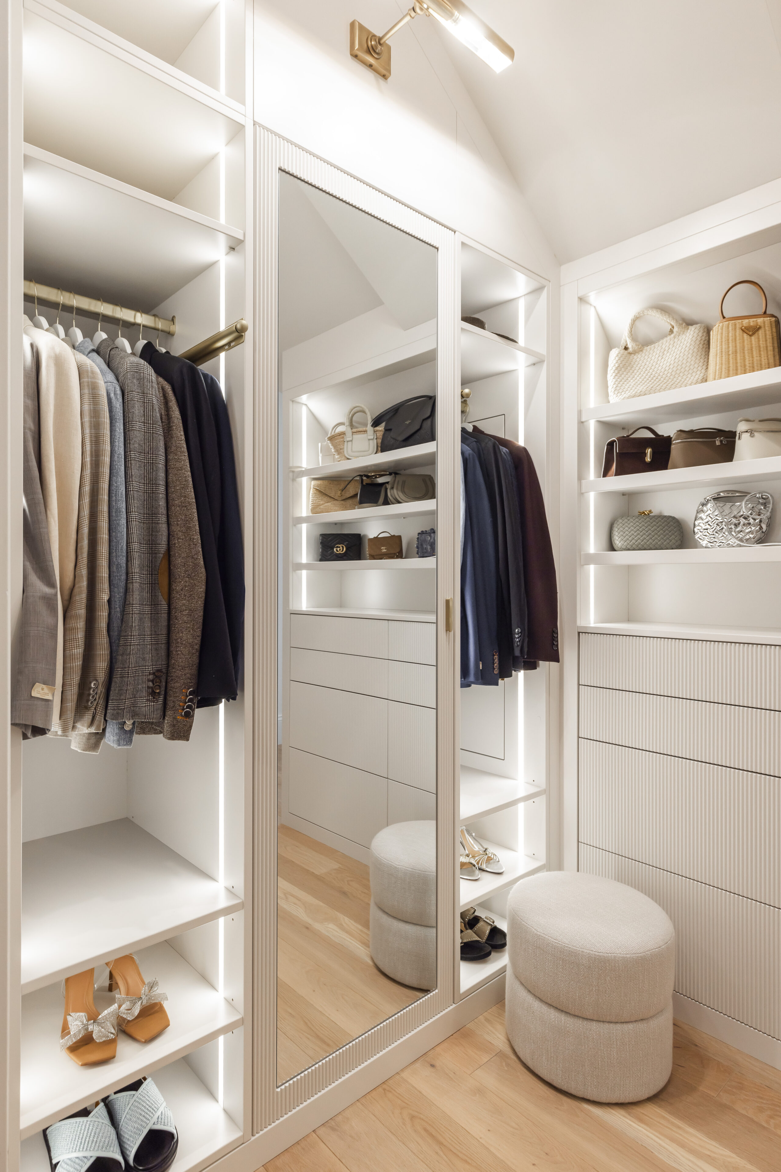 Discover an elegant walk-in closet featuring organized clothing, a full-length mirror, and a cozy ottoman for a stylish dressing experience.