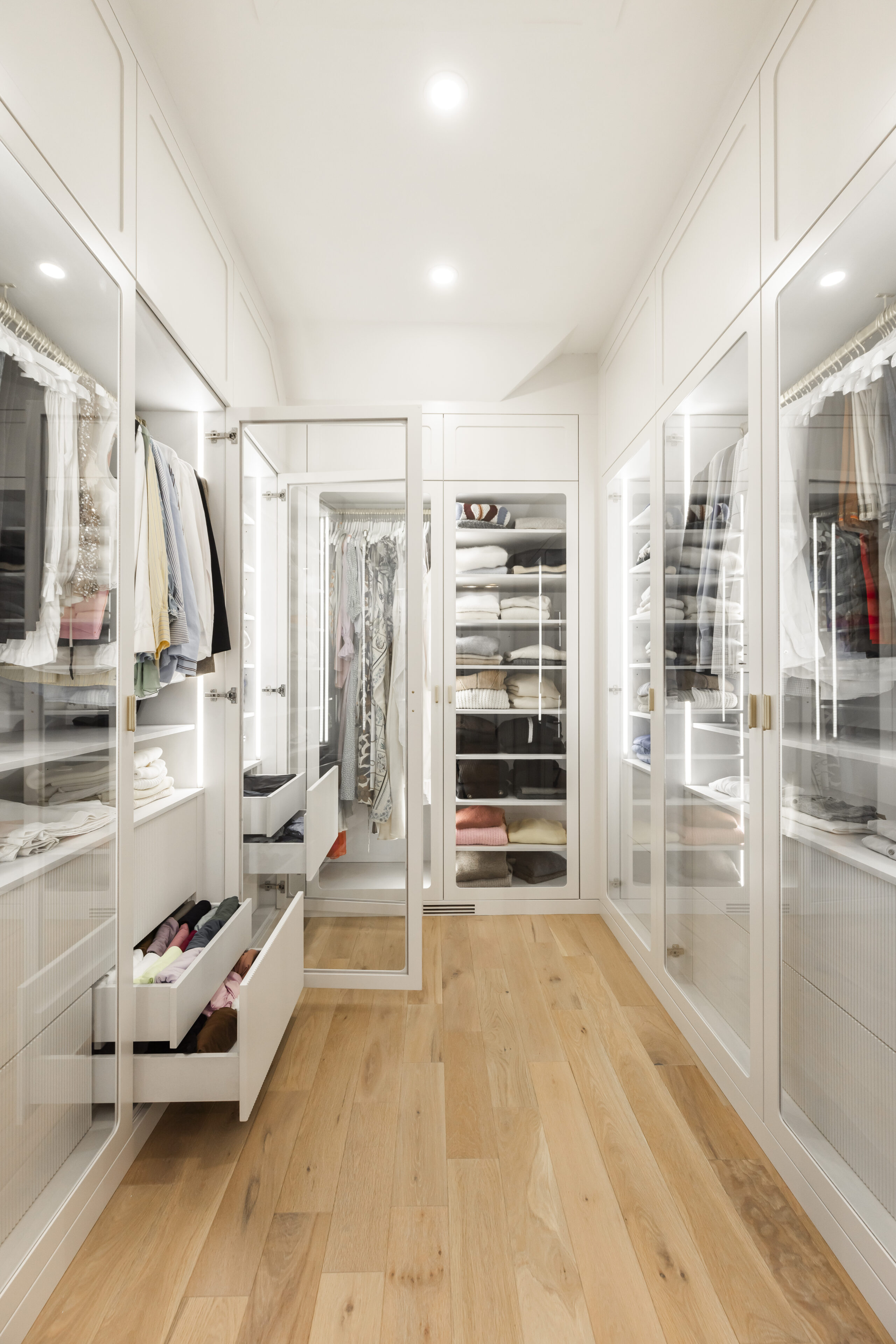 Experience modern elegance in this beautifully organized walk-in closet, featuring glass cabinetry and a spacious, bright layout.