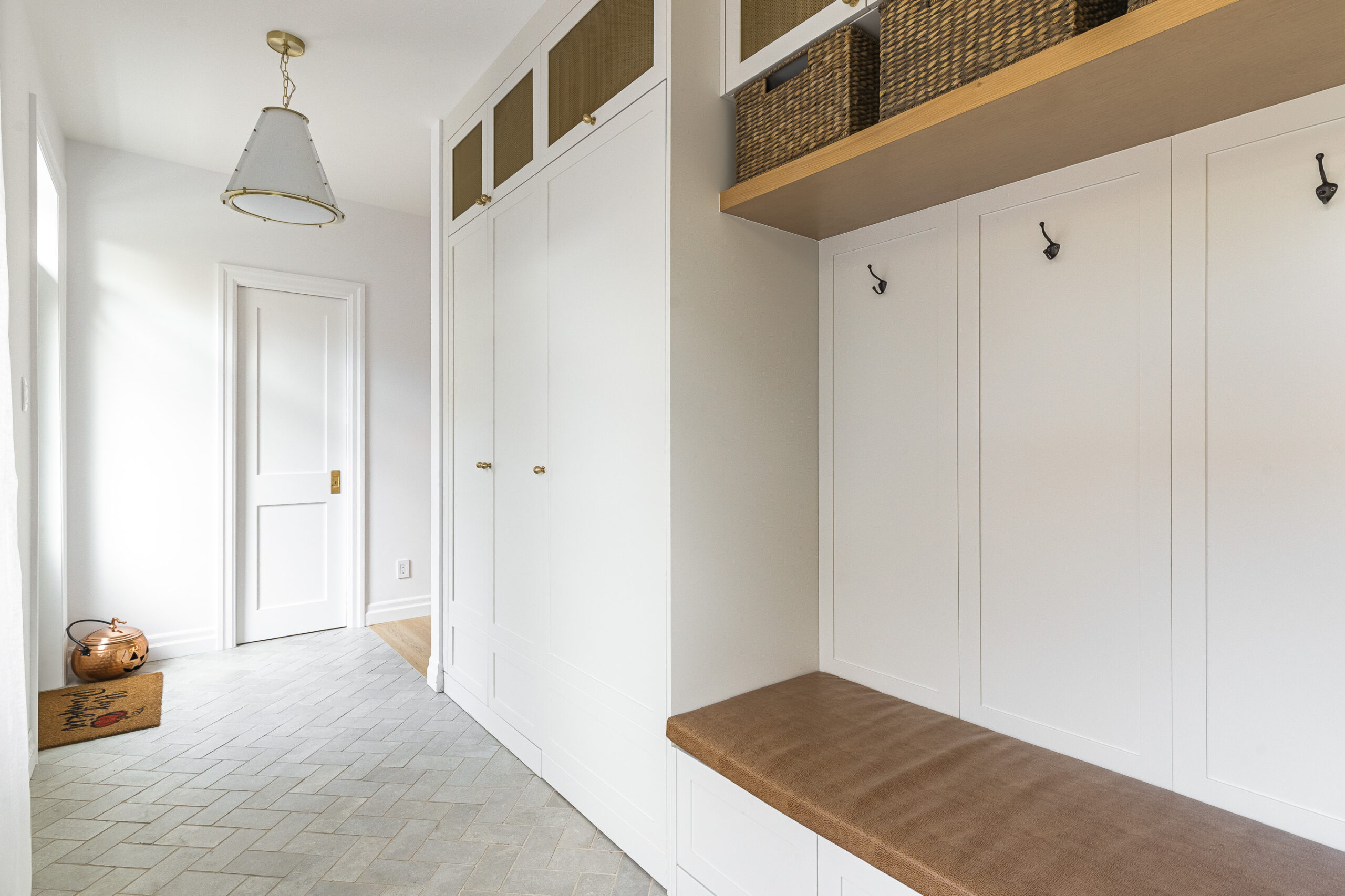 Bright and inviting entryway featuring minimalist design, a functional bench, woven baskets, and elegant herringbone tiles.