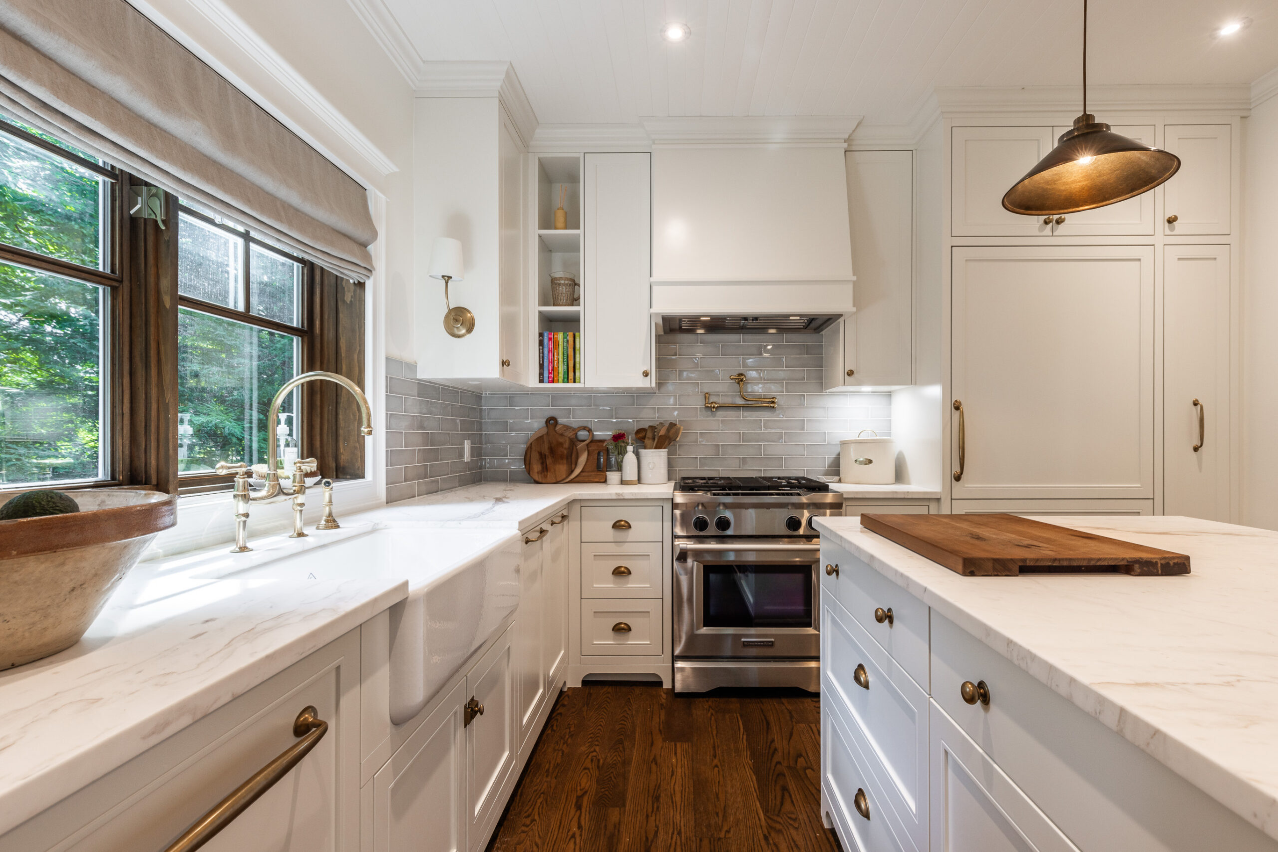 A sophisticated white kitchen with marble countertops, brass accents, and natural light flooding in through large windows creates an inviting atmosphere.