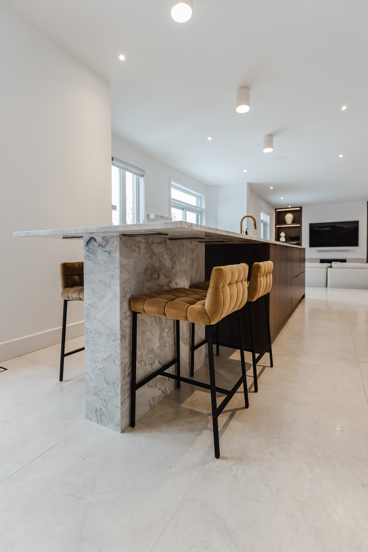 Bright and elegant modern kitchen featuring a stylish island, chic tan chairs, and abundant natural light for a welcoming atmosphere.