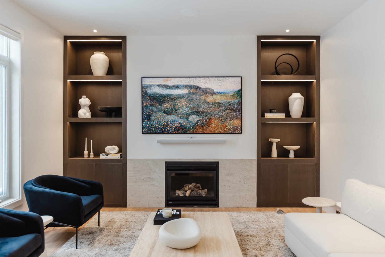 A stylish contemporary living room features deep blue accents, elegant shelves, and a modern fireplace for a cozy, inviting atmosphere.
