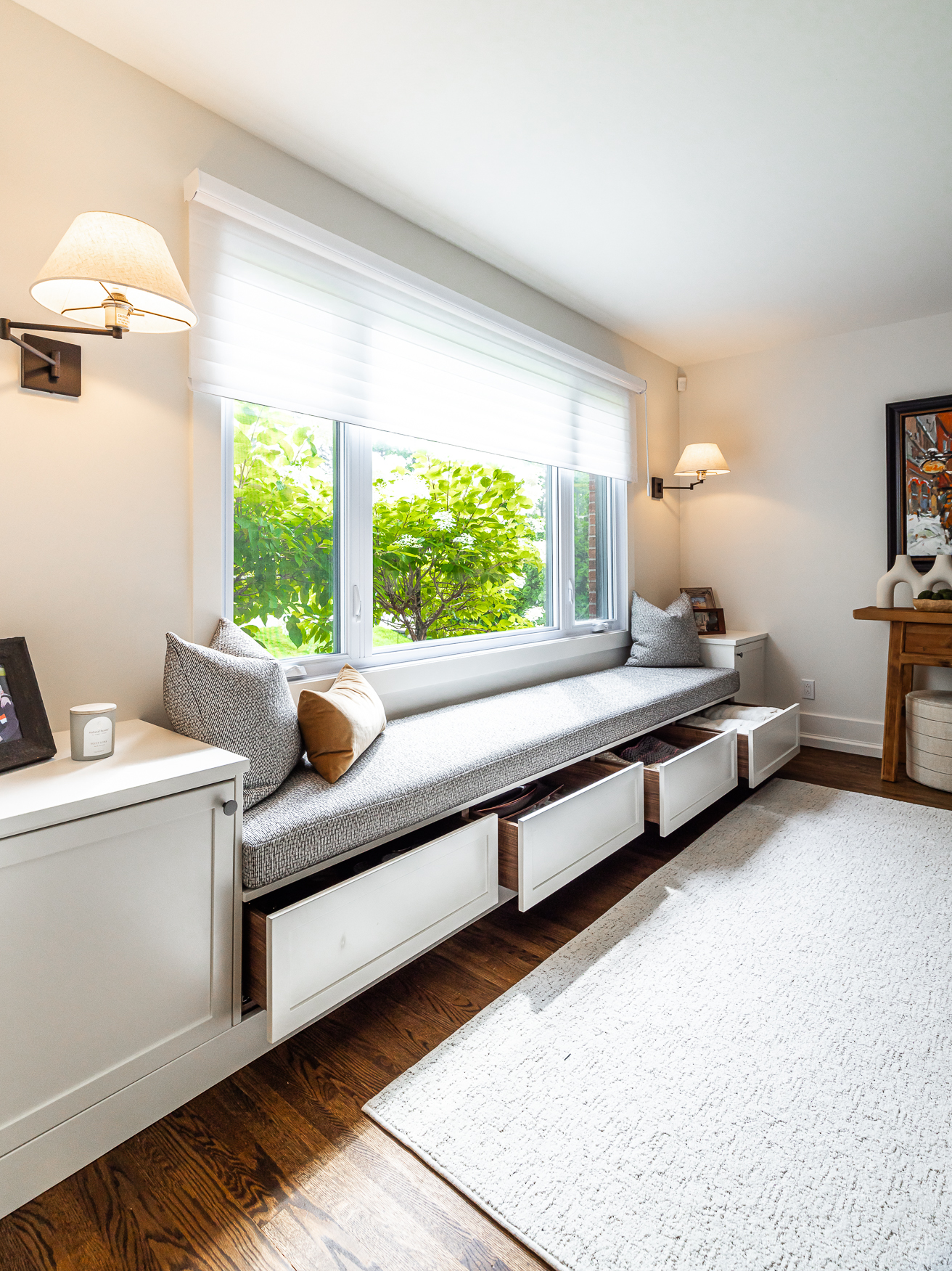 A cozy living room features a stylish window seat with soft cushions, bright natural light, and practical storage options for a warm retreat.