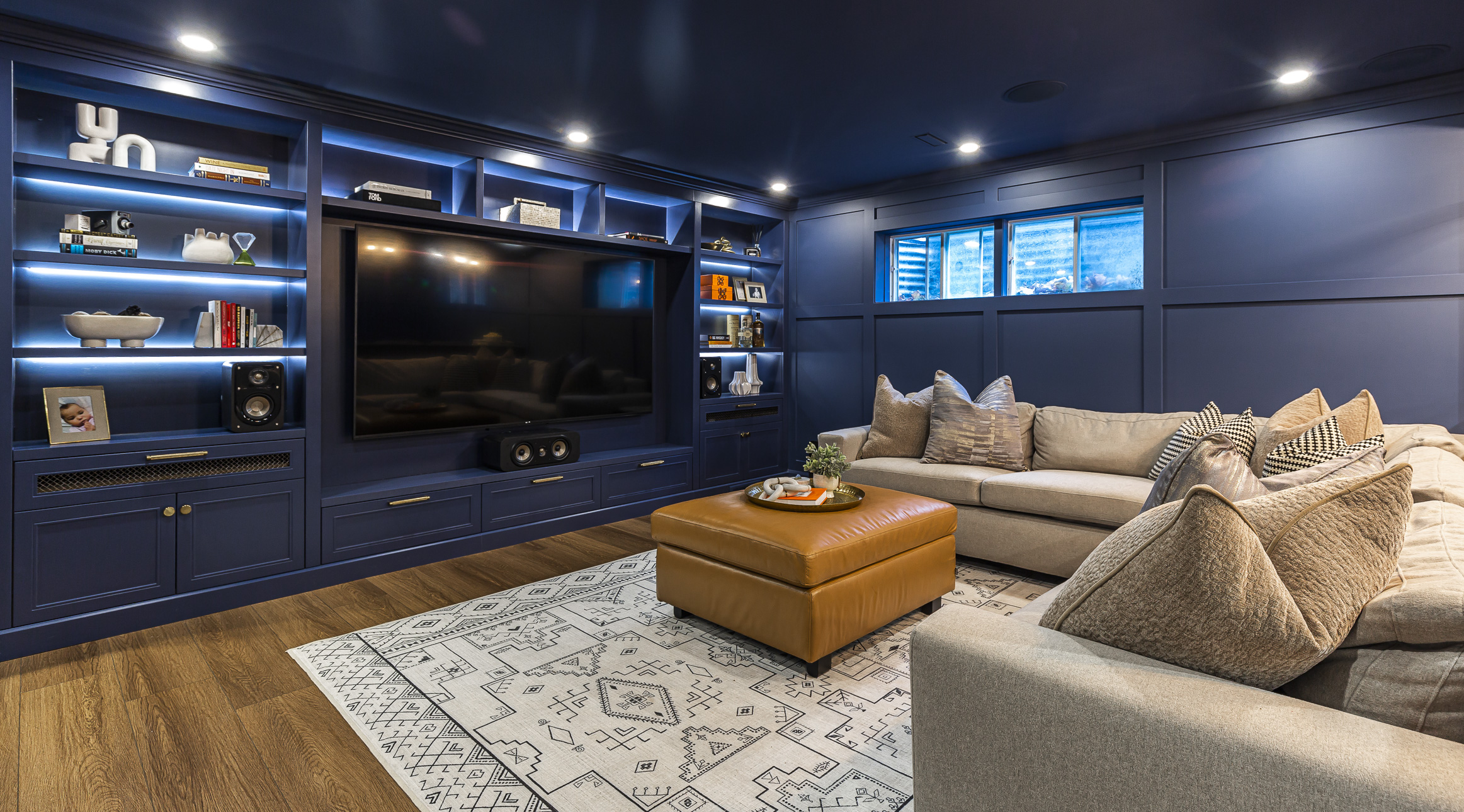 Chic entertainment room featuring navy walls, a cozy sectional, and inviting lighting, perfect for movie nights and relaxing gatherings.