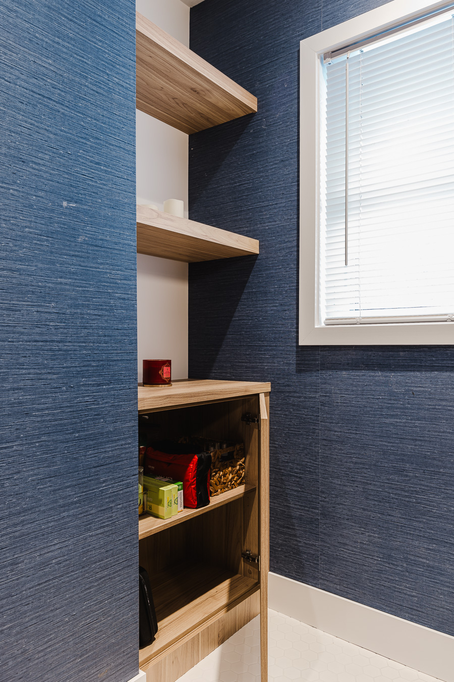 Cozy storage nook featuring navy wallpaper, light wooden shelves, and natural light for a warm and inviting atmosphere.