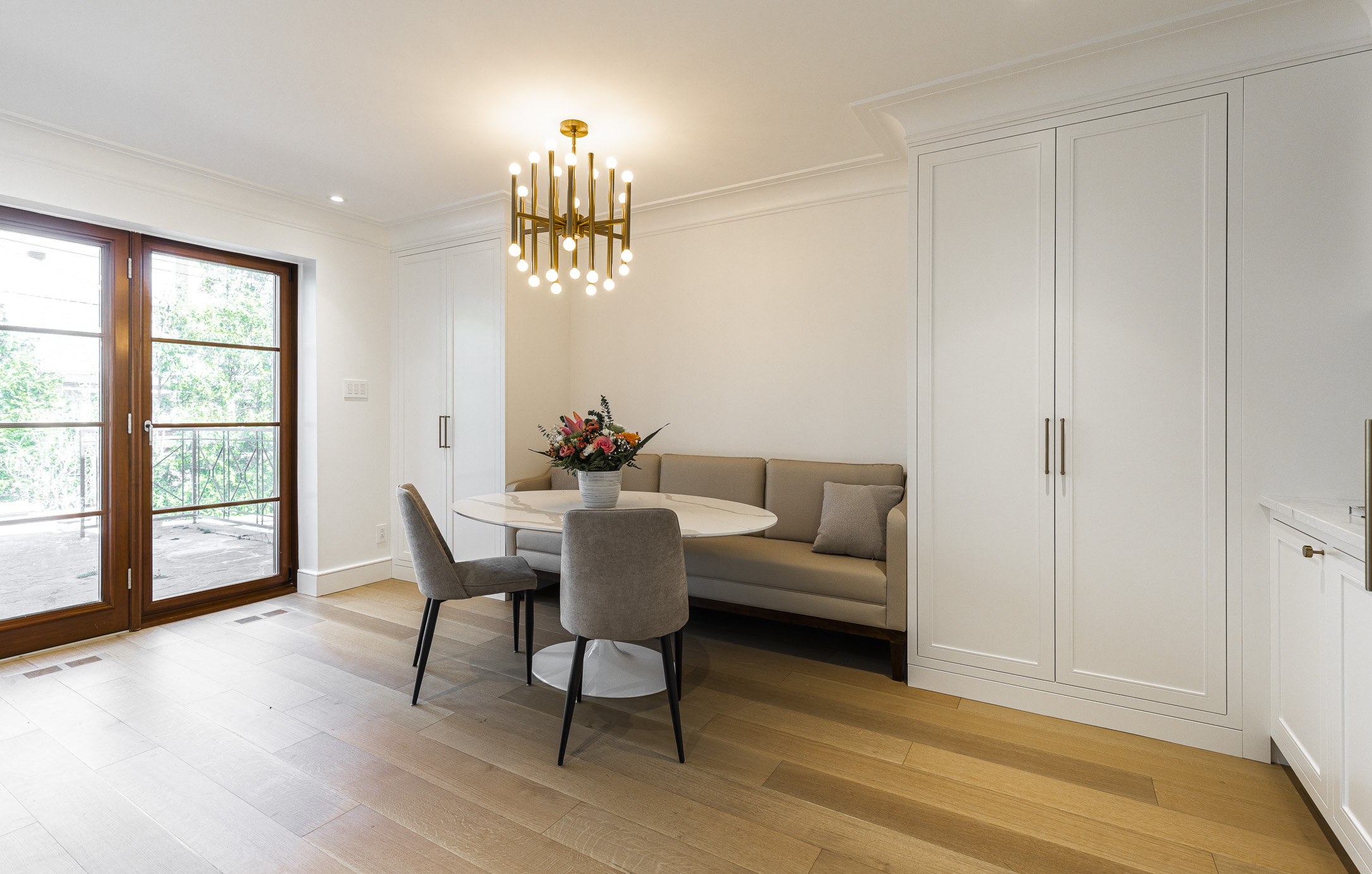Elegant modern dining area featuring a round table, plush chairs, and natural light from double doors leading to outdoor greenery.